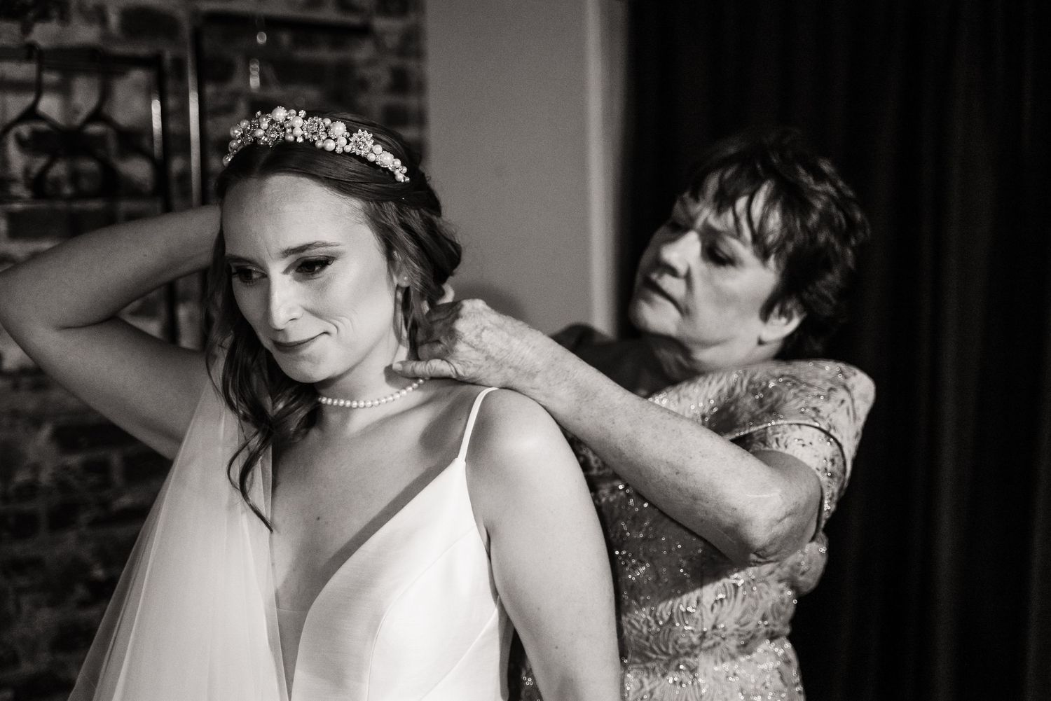 A black and white photo shows a bride getting help with final preparations before her wedding ceremony.