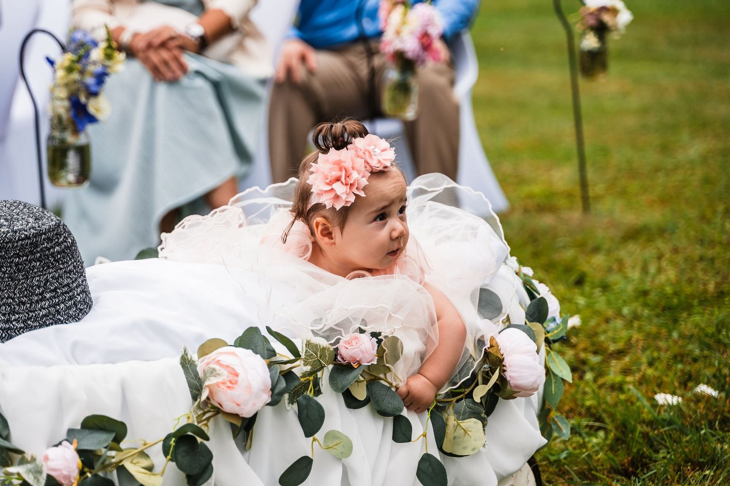 Baby flower girl in decorated wagon with floral garlands at outdoor wedding.