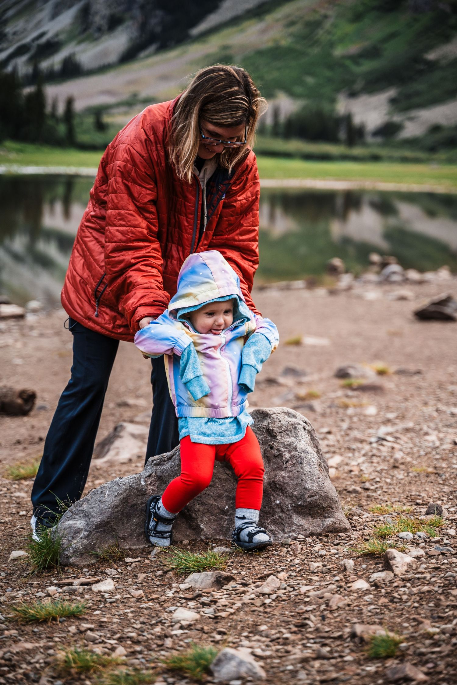 A family explores the rocky shoreline of an alpine lake on a cloudy mountain day.