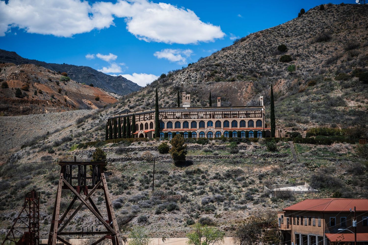 Historic mine buildings and structures nestled into rugged mountain terrain under bright blue skies in the American West.