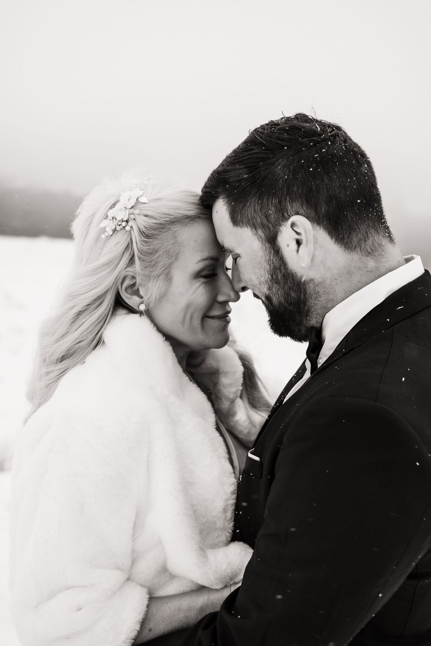 An intimate black and white wedding portrait showing a tender moment between newlyweds in winter attire.
