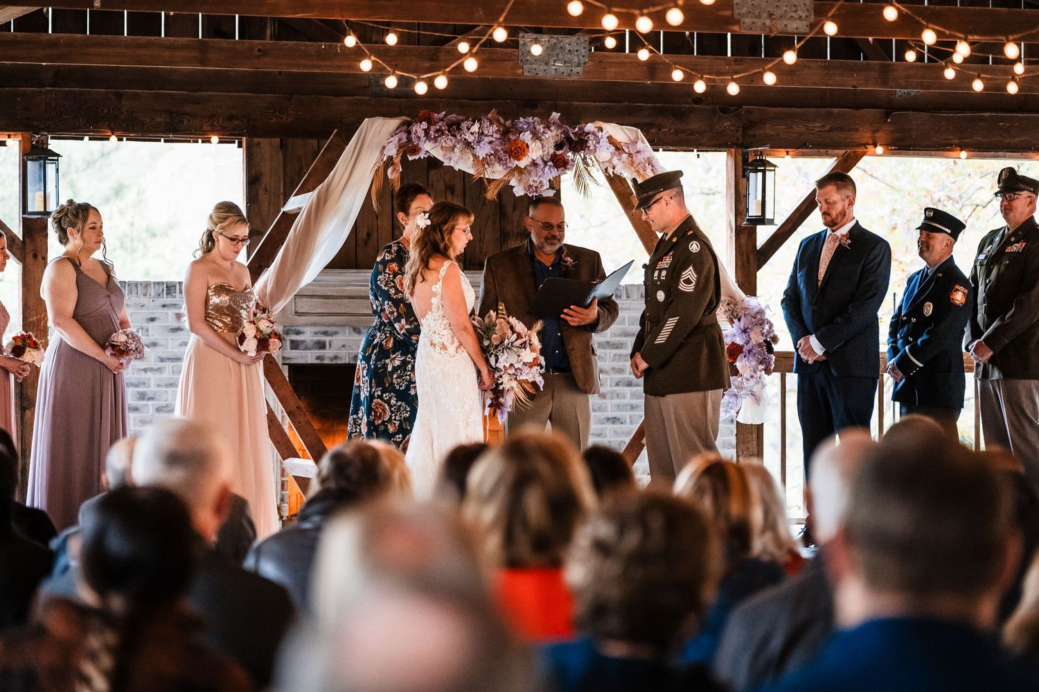 A wedding ceremony in progress under a covered venue with string lights and gathered guests.