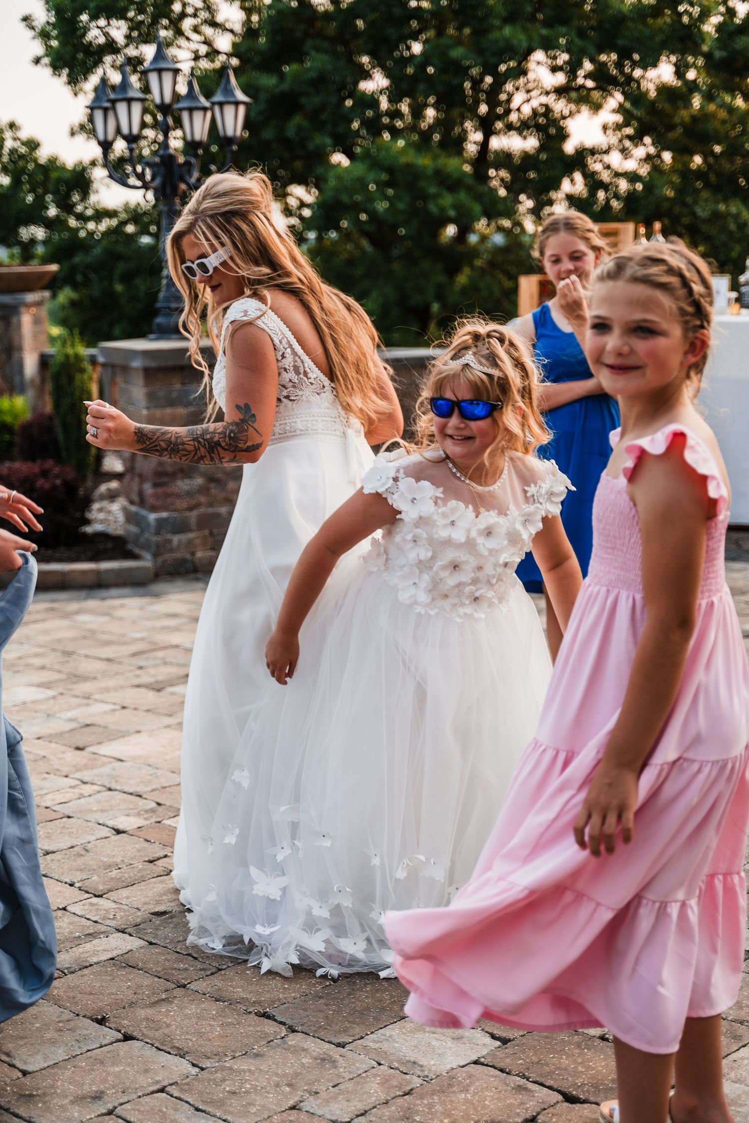 Children in formal dresses dancing and celebrating at an outdoor wedding reception.