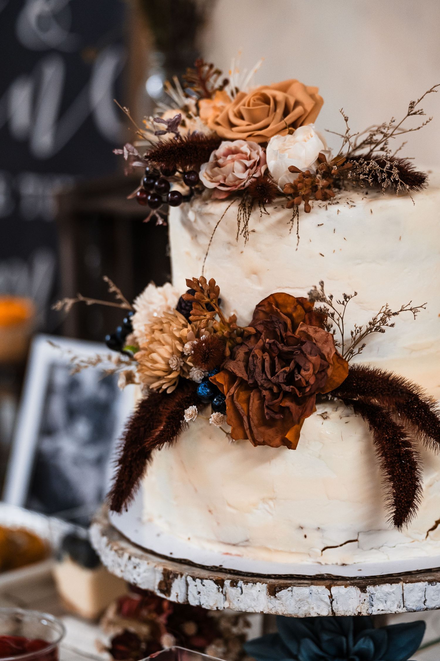 Elegant white wedding cake decorated with dried brown flowers and natural elements.