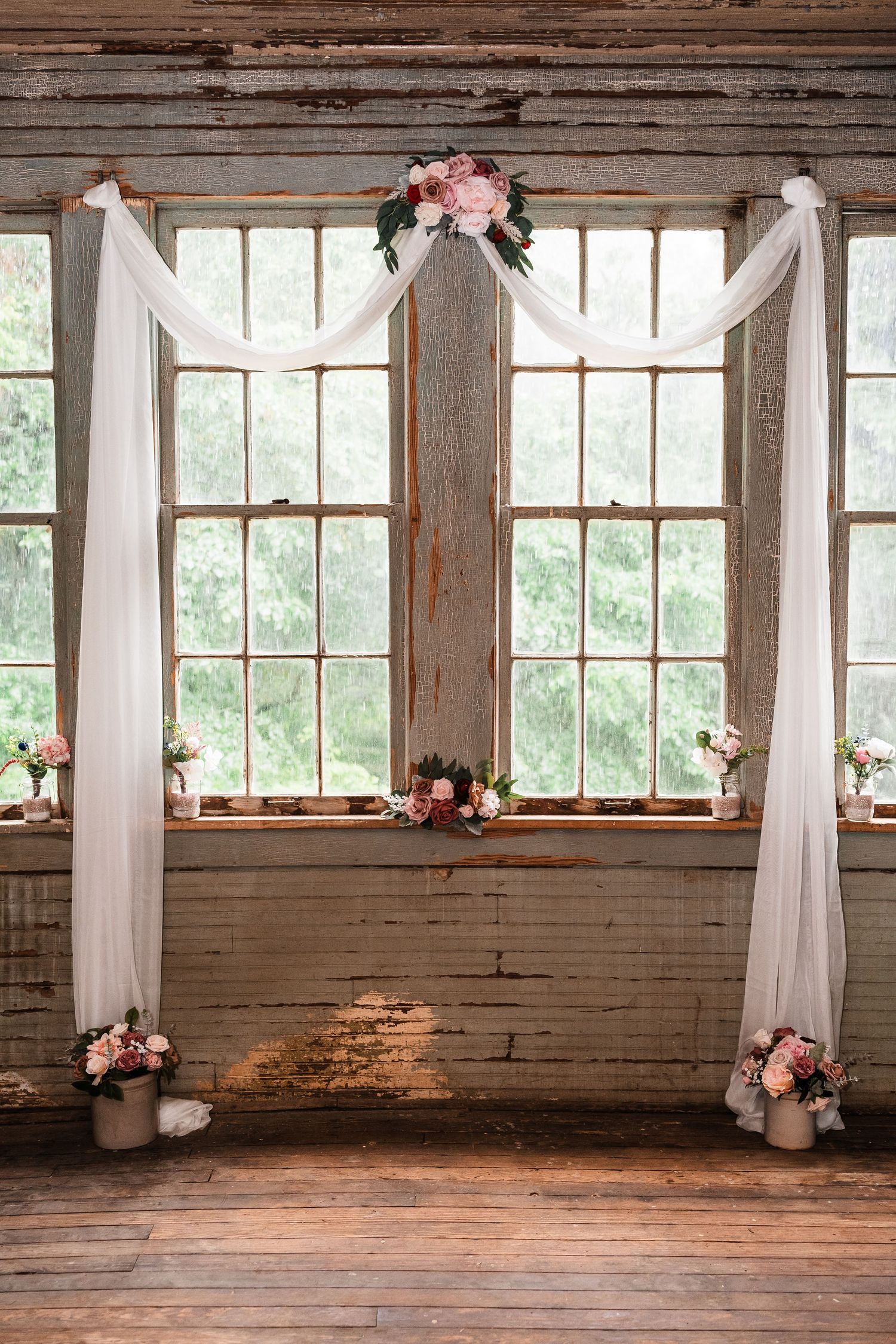 Rustic indoor venue with white drapes and wooden floors illuminated by natural window light.