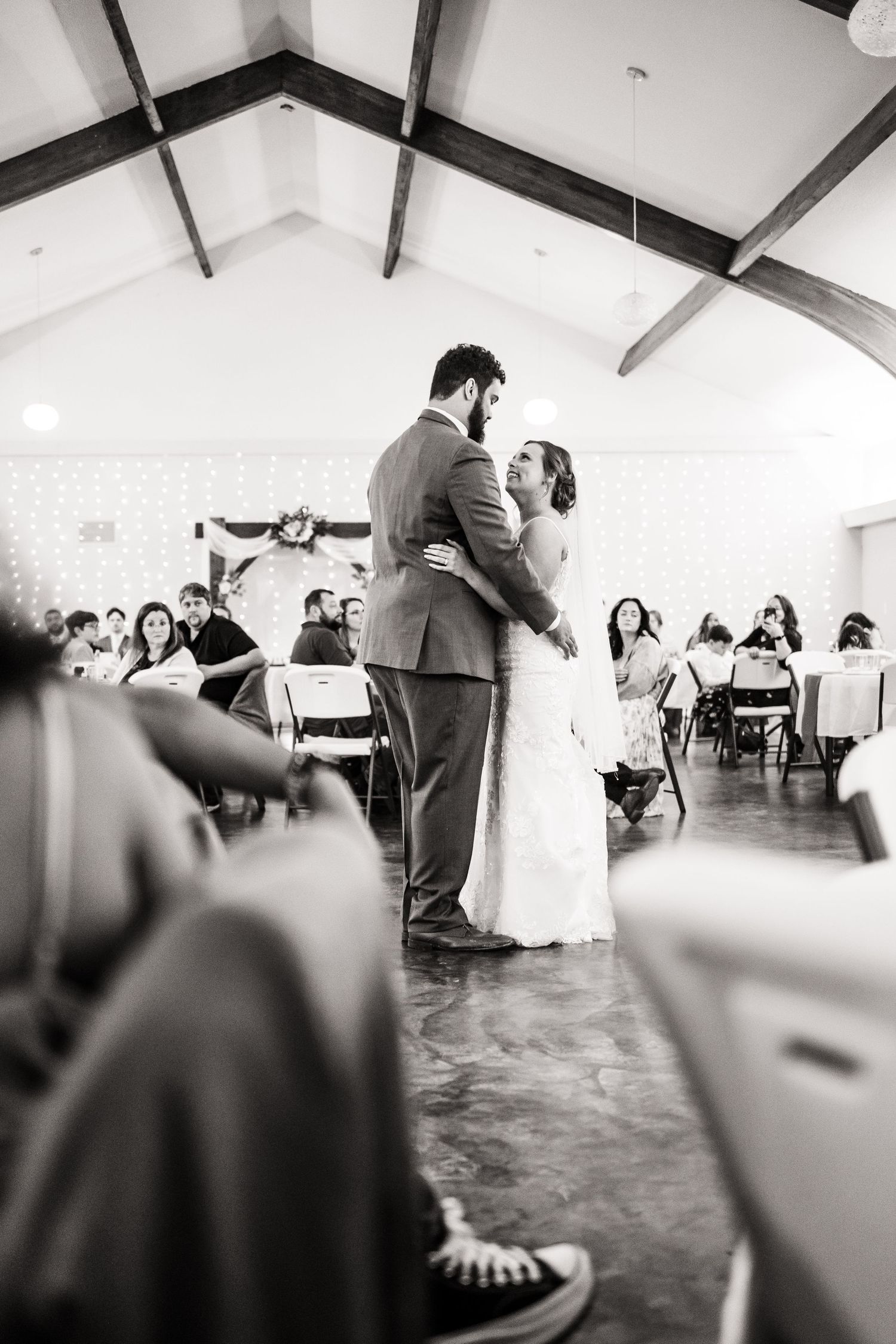 A couple shares their first dance at a wedding reception as guests watch from their seats in a bright venue with vaulted ceilings.