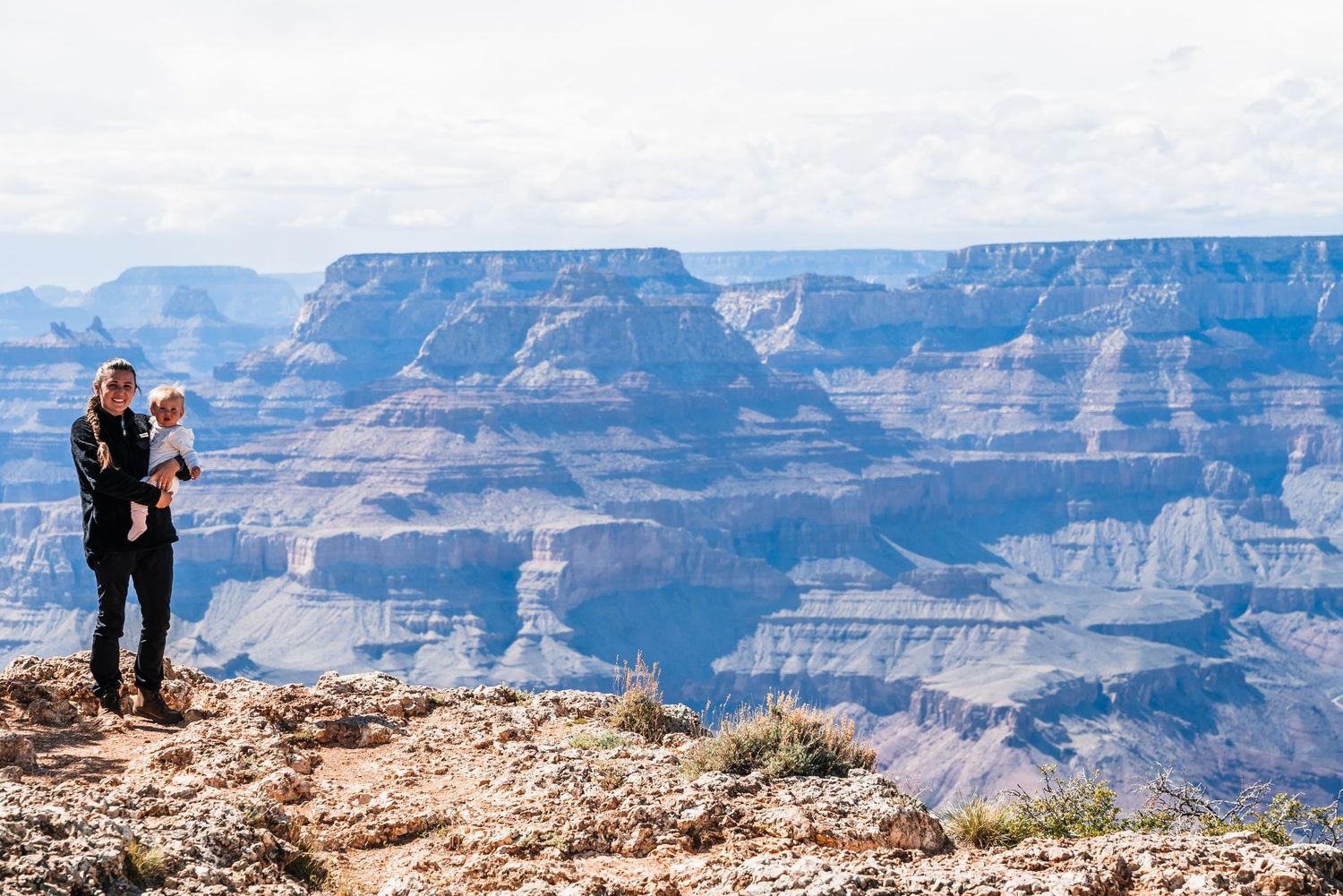 Scenic overlook at Grand Canyon showing vast layered cliffs and deep valleys against blue sky.