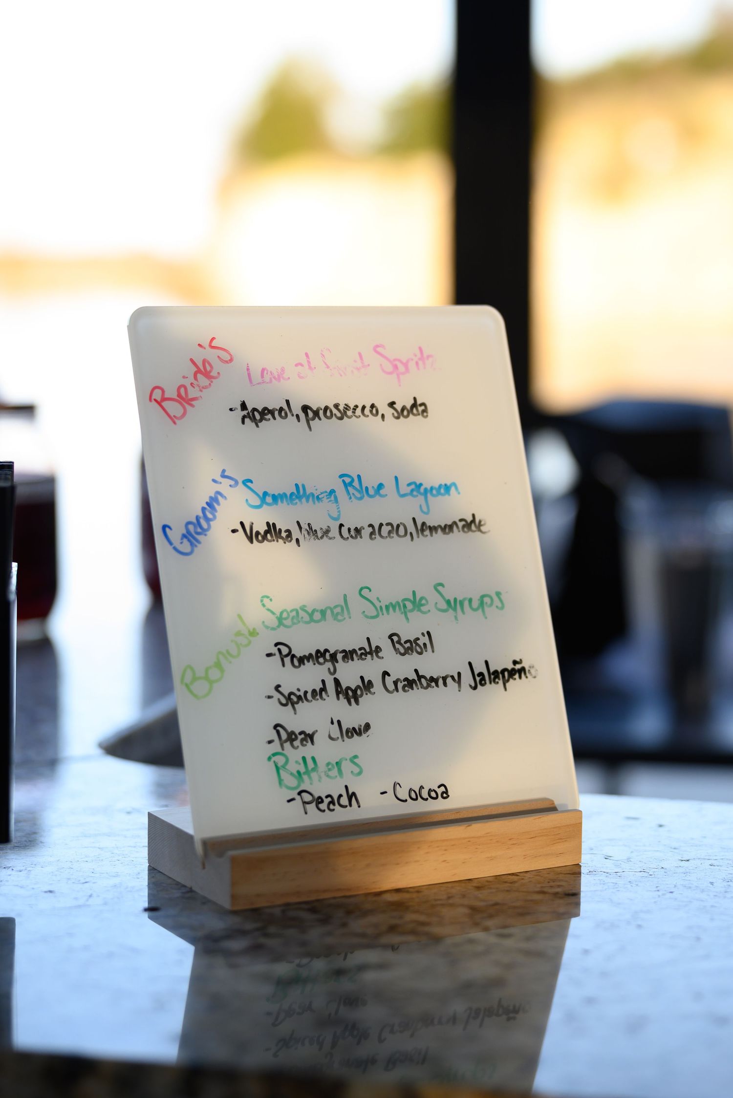 Handwritten drink menu cards displayed on wooden stands at wedding bar.