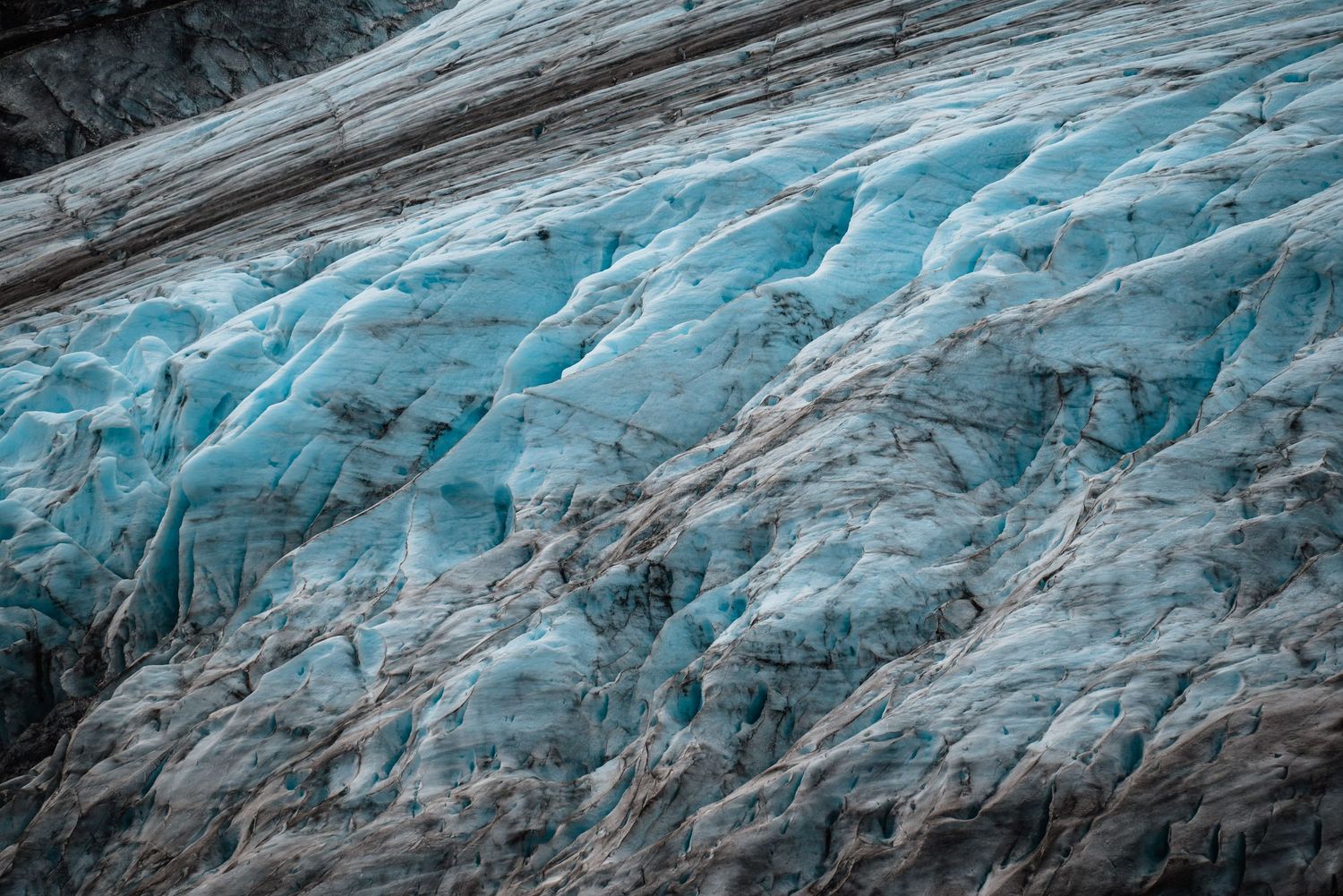 Close-up view of a glacier's blue ice formations with striations and crevasses visible in the frozen surface.