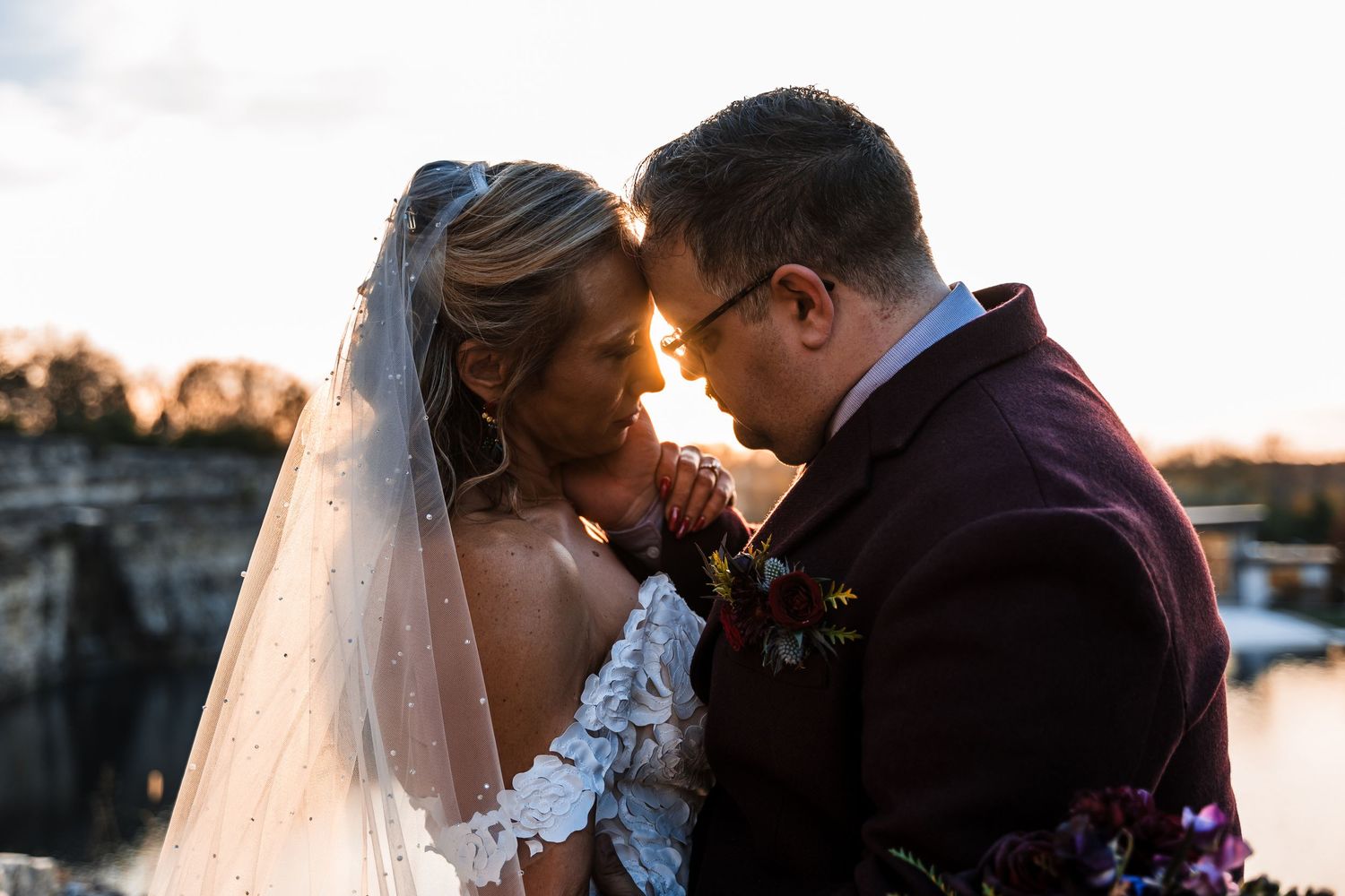 A romantic sunset wedding moment between a couple in formal attire with the bride wearing a white veil.
