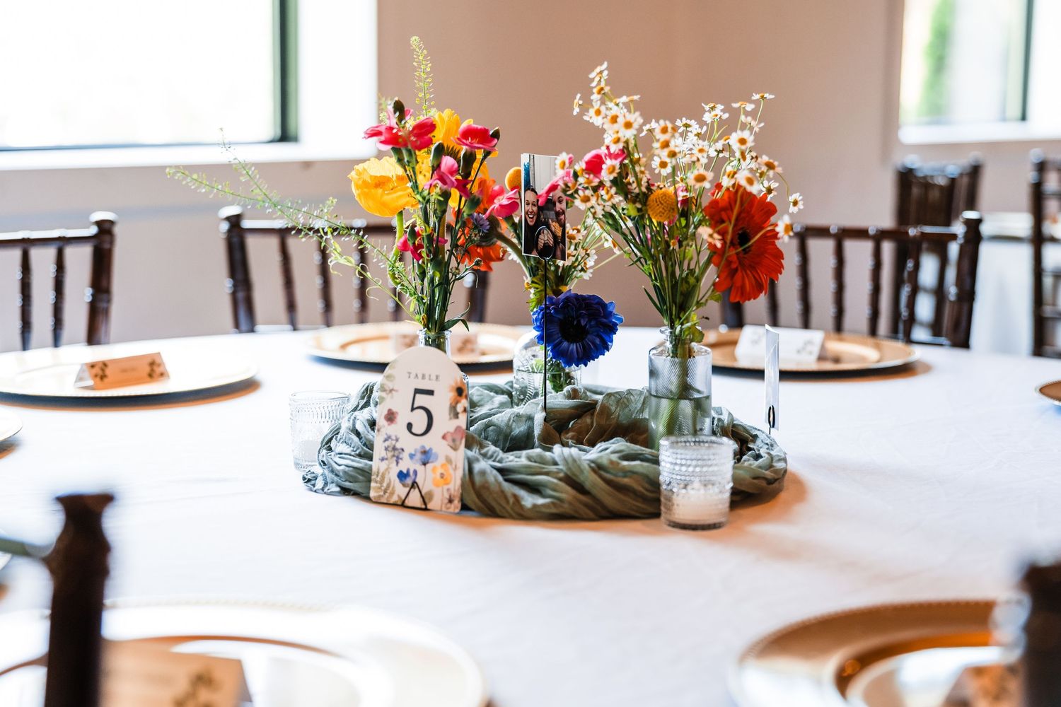 Colorful wildflower centerpieces in glass vases surround table number five at an elegant wedding reception.
