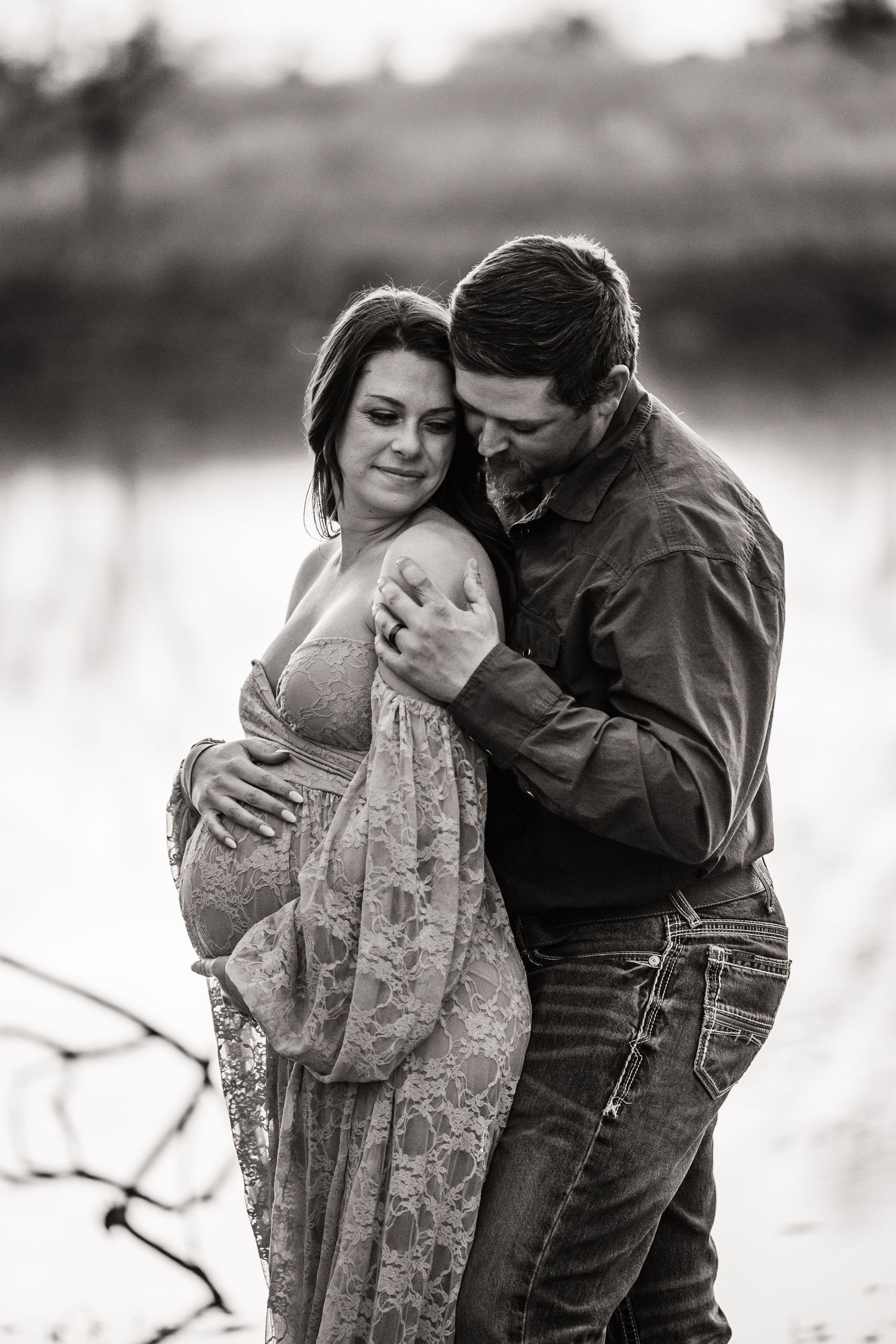 A romantic black and white photo series shows a couple embracing by a lake in intimate candid moments.