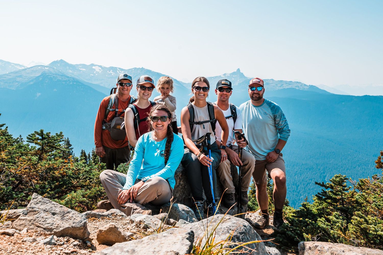 Hikers resting on mountain summit with panoramic views of distant peaks.