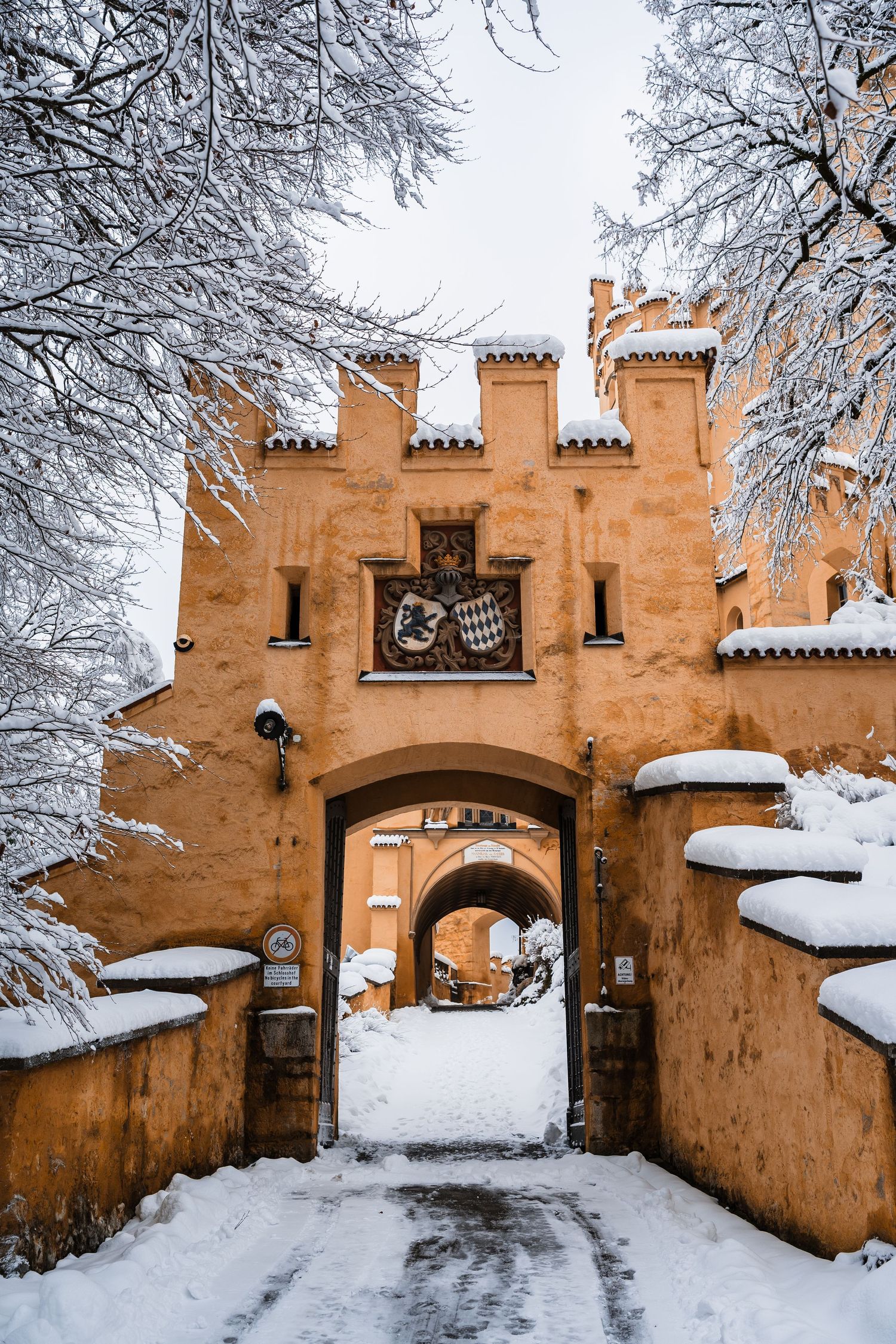 Snow covered entrance to a medieval castle with orange stone walls and turrets in winter.