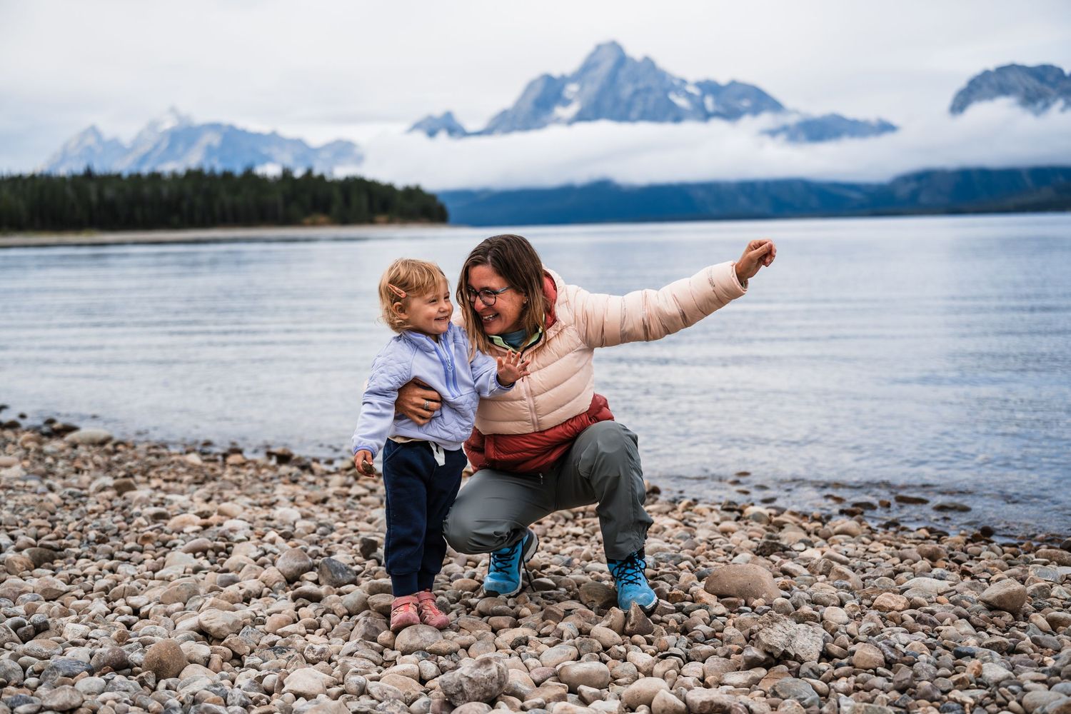Family exploring a rocky beach shoreline with mountains and cloudy skies in the background.
