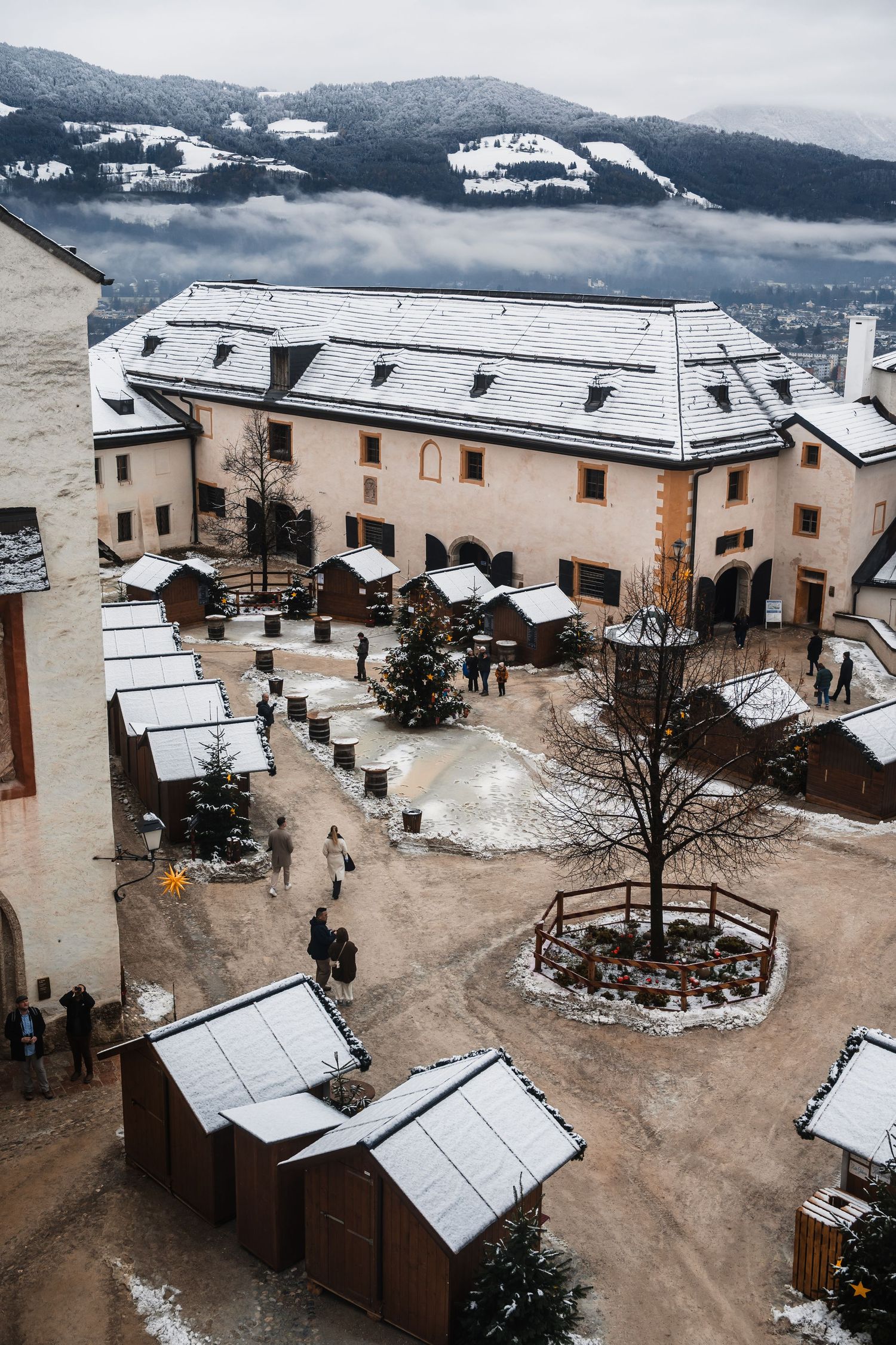 Aerial view of a snow-covered courtyard surrounded by beige buildings in a mountainous setting.