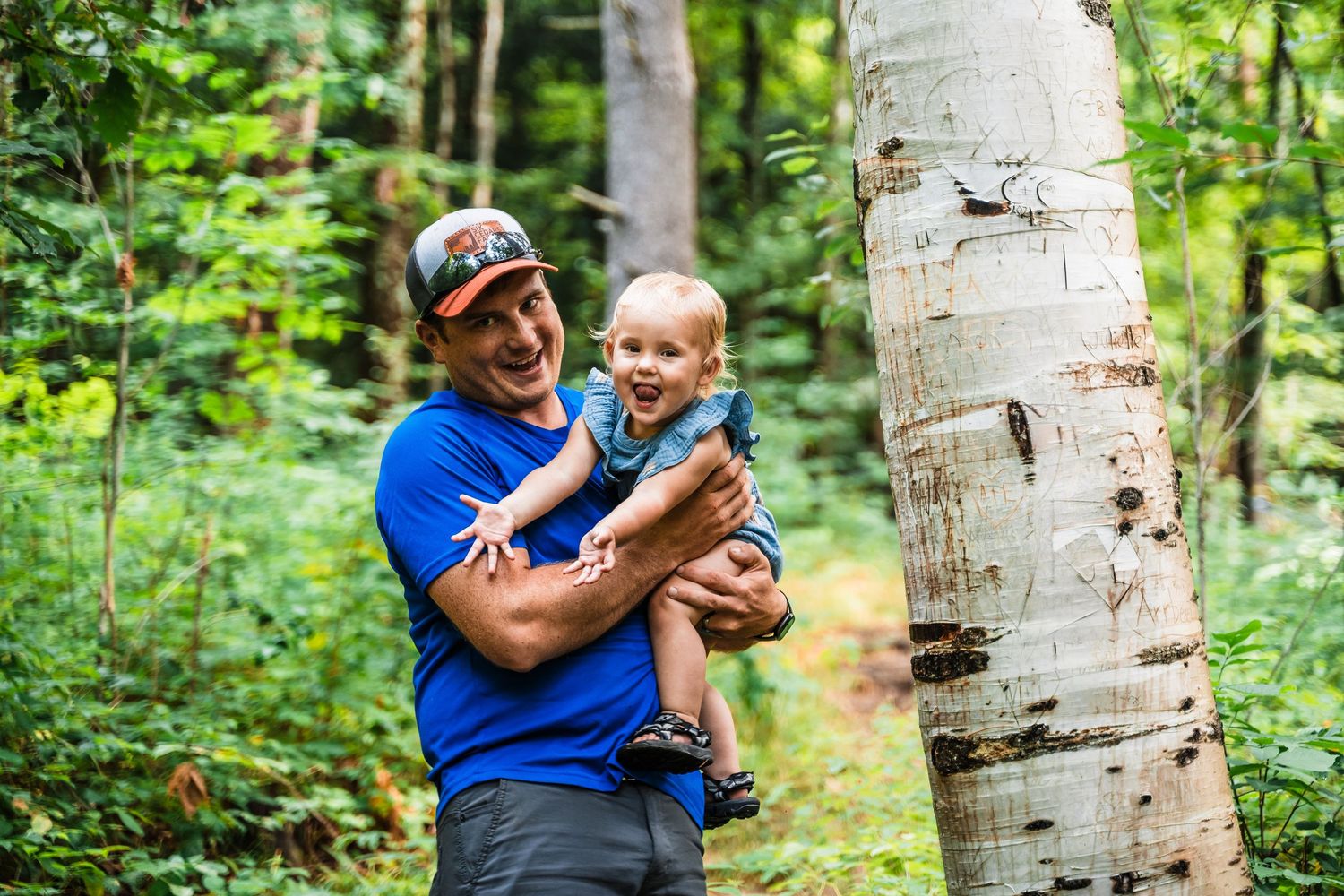A joyful moment shared between two people near a birch tree in a forest setting.