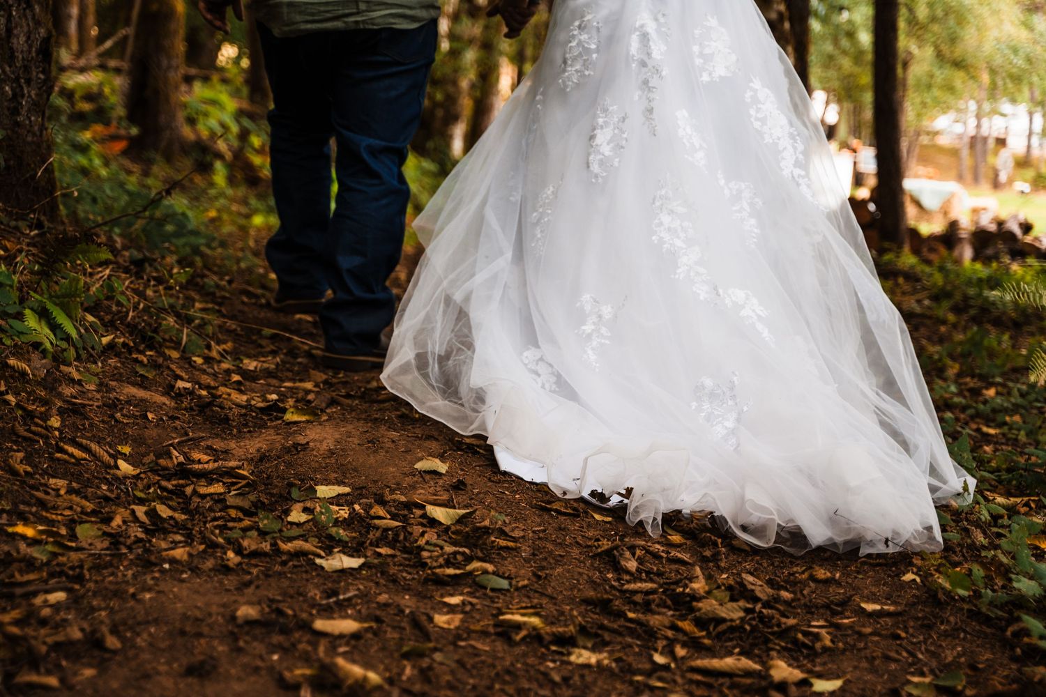 White wedding dress train trailing on forest path during outdoor ceremony.