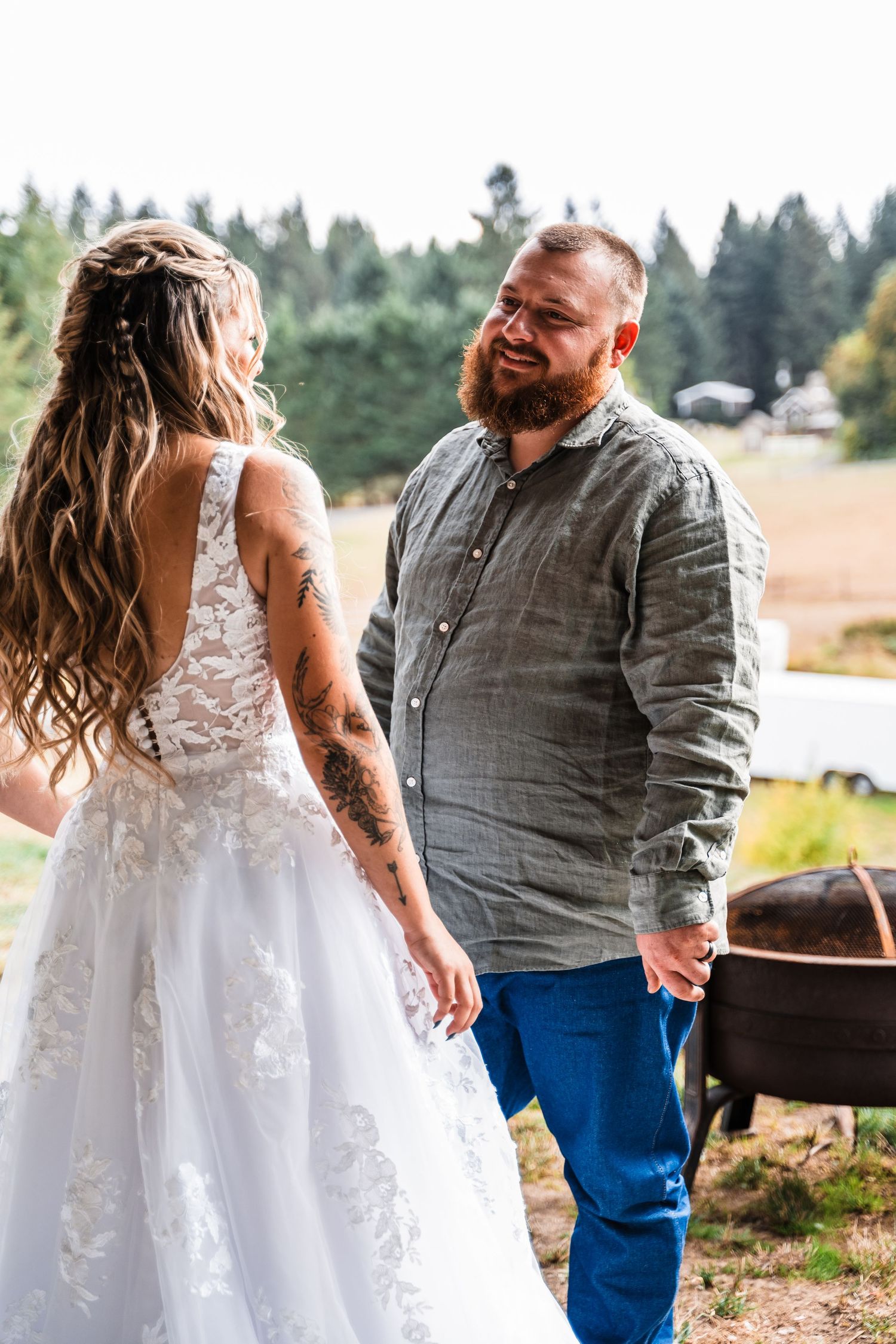 A couple shares a candid moment outdoors during a rustic country wedding, with evergreen trees in the background.