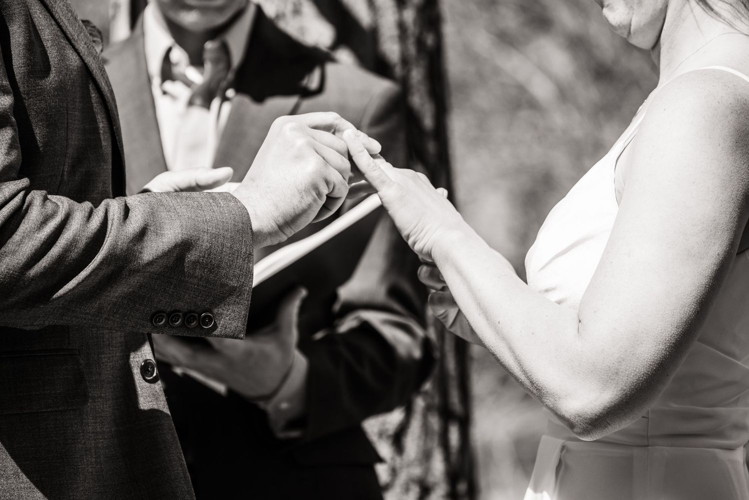 Close-up black and white shot of hands exchanging wedding rings during a ceremony.