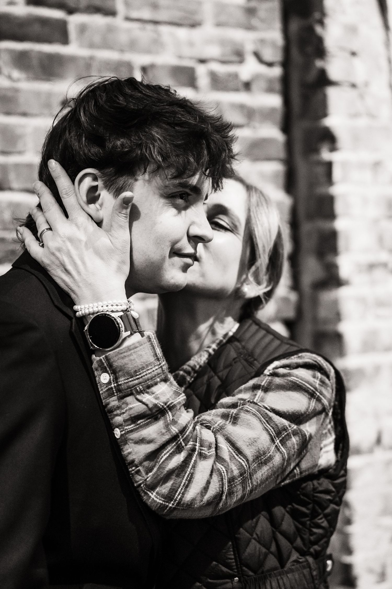 Intimate black and white portrait of a couple sharing a tender moment against a brick wall.
