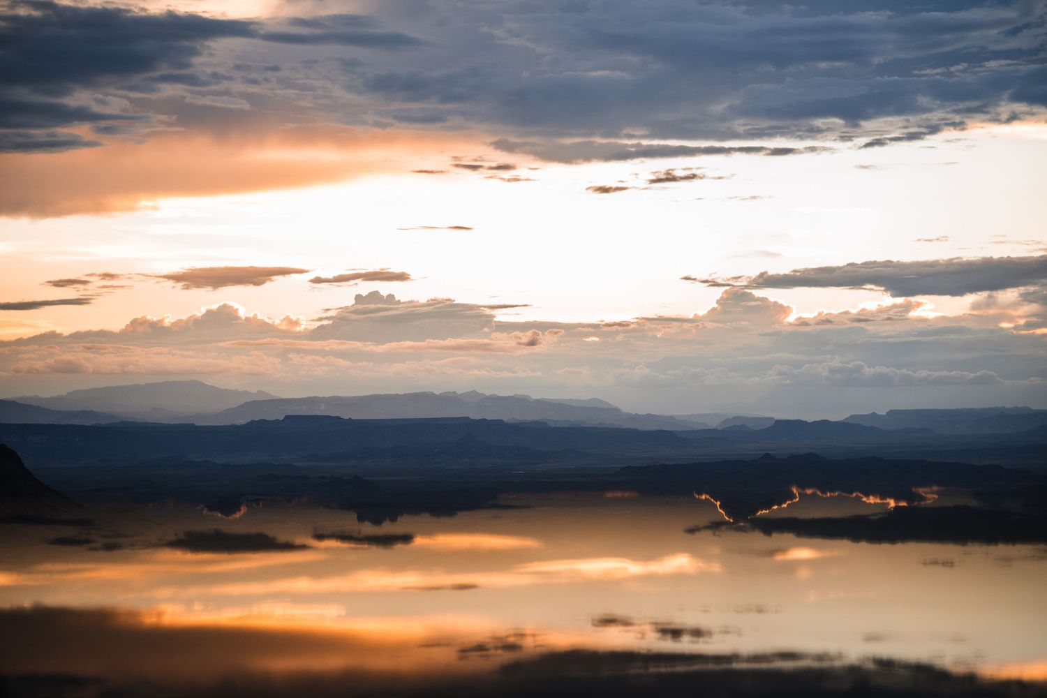 Stunning sunset over a mountain lake with orange clouds reflecting on calm waters.
