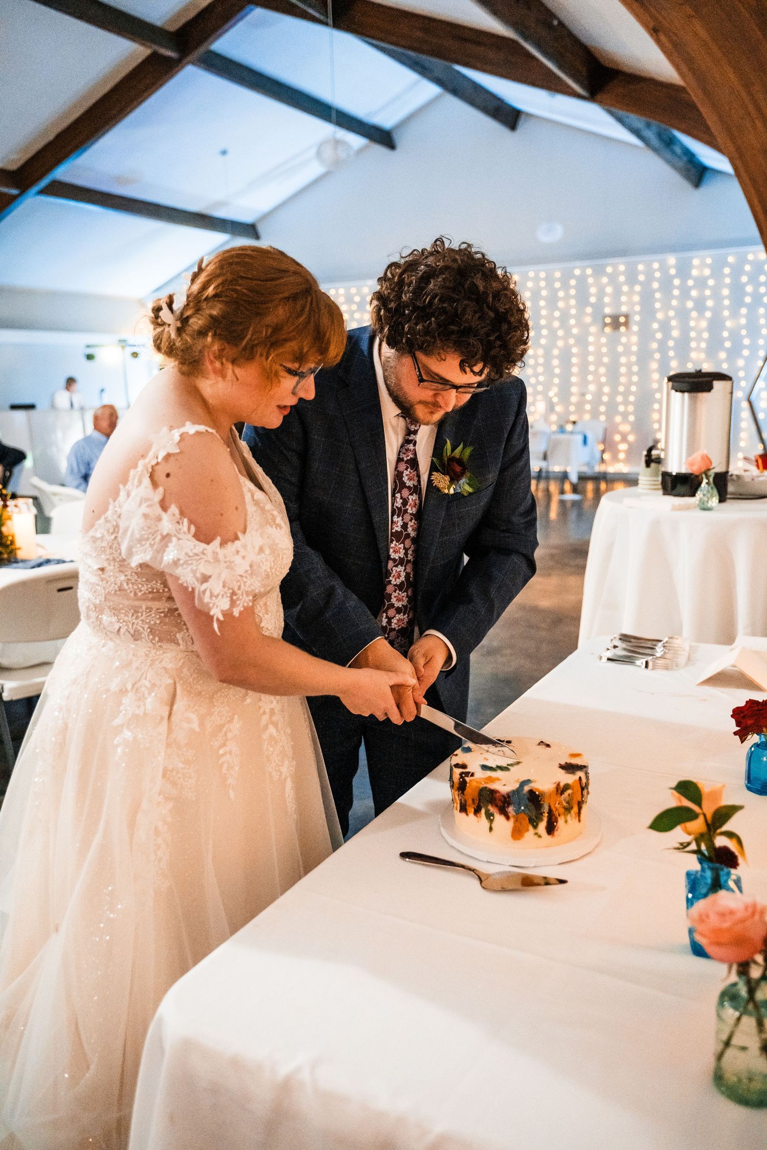 Couple cuts their wedding cake together at a reception decorated with twinkle lights.