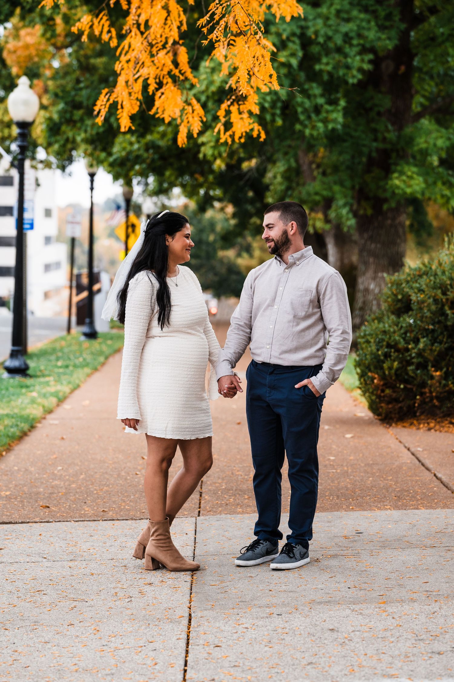 Couple holding hands while walking on path under golden autumn leaves.