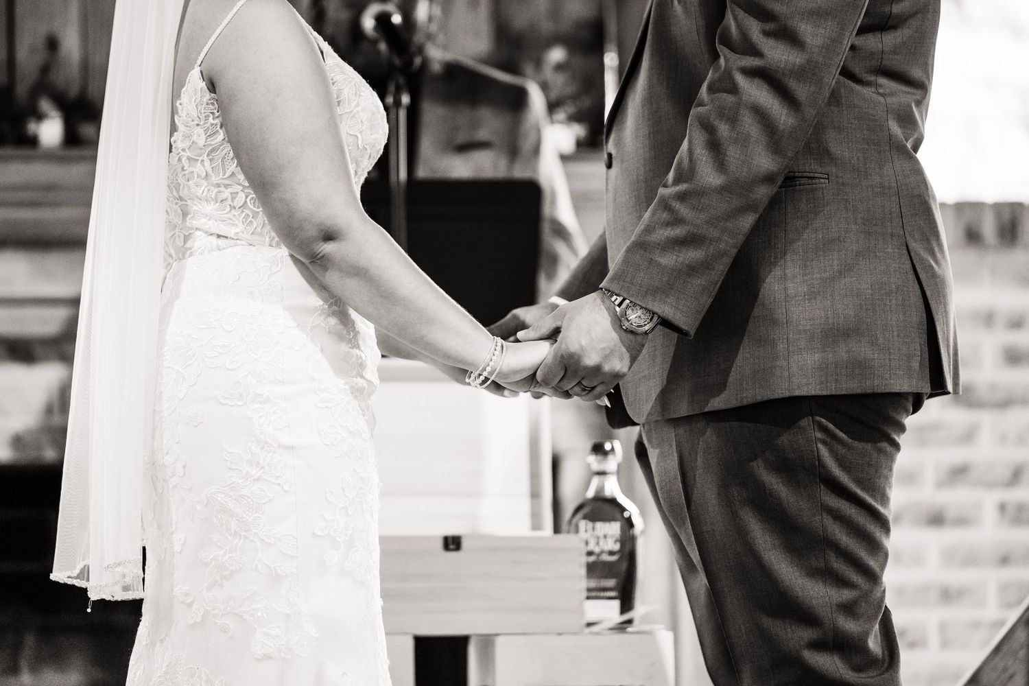 Black and white photo capturing couple holding hands during wedding ceremony.