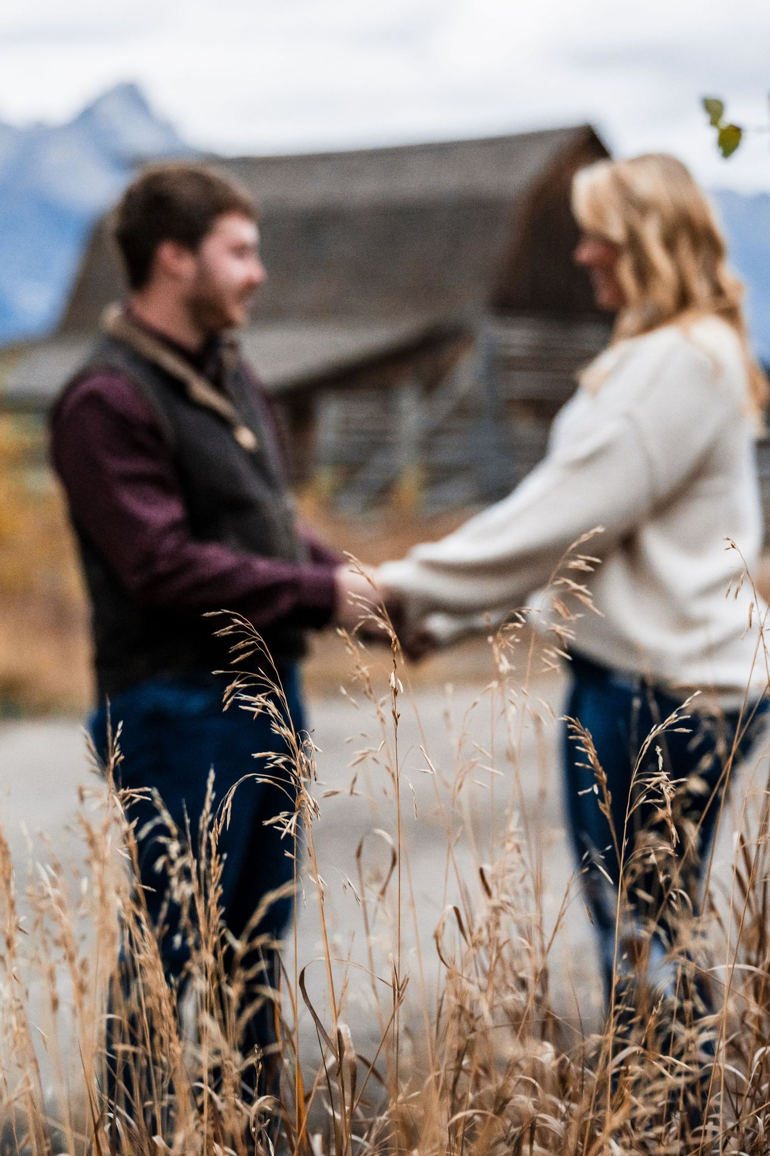 Couple sharing an intimate moment in front of mountain peaks with tall grass in the foreground.