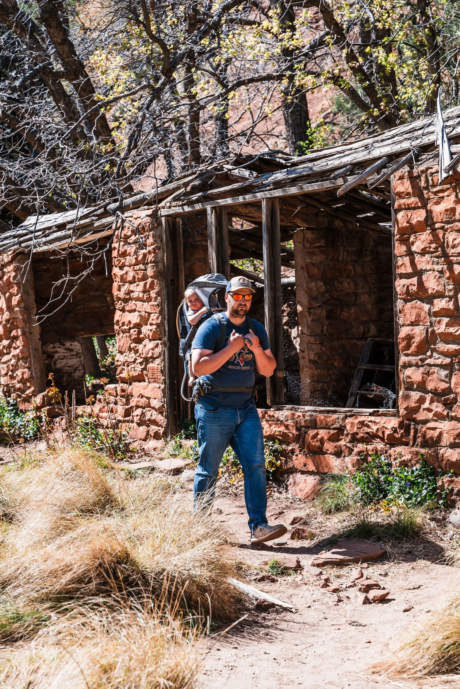Hiker wearing backpack and cap explores old rustic stone ruins along desert trail in national park.