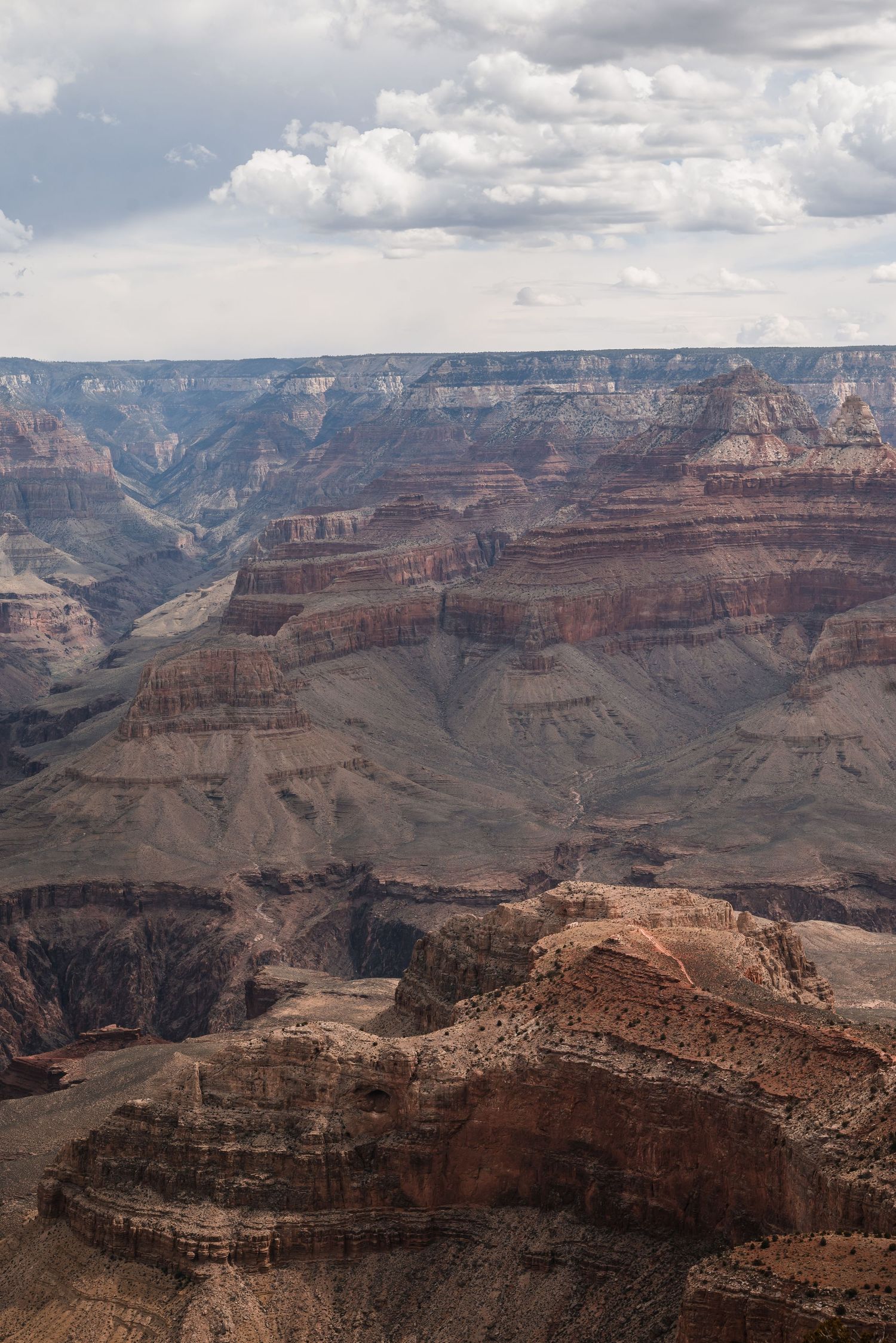 Dramatic layered cliffs and deep canyons of the Grand Canyon under a cloudy sky with sunlight illuminating the rock formations.