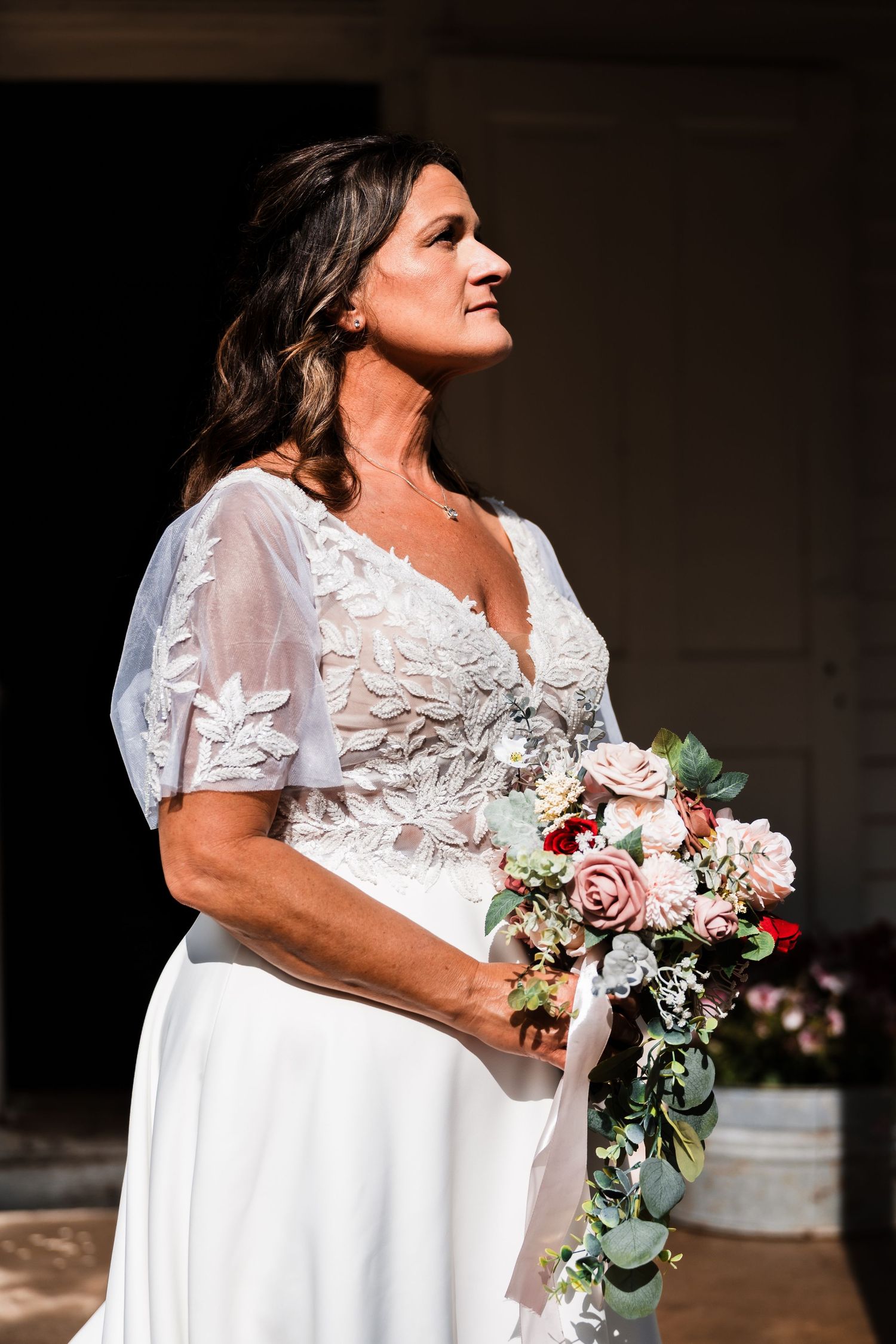 Bride in white lace dress holding elegant bouquet of pink and white flowers.