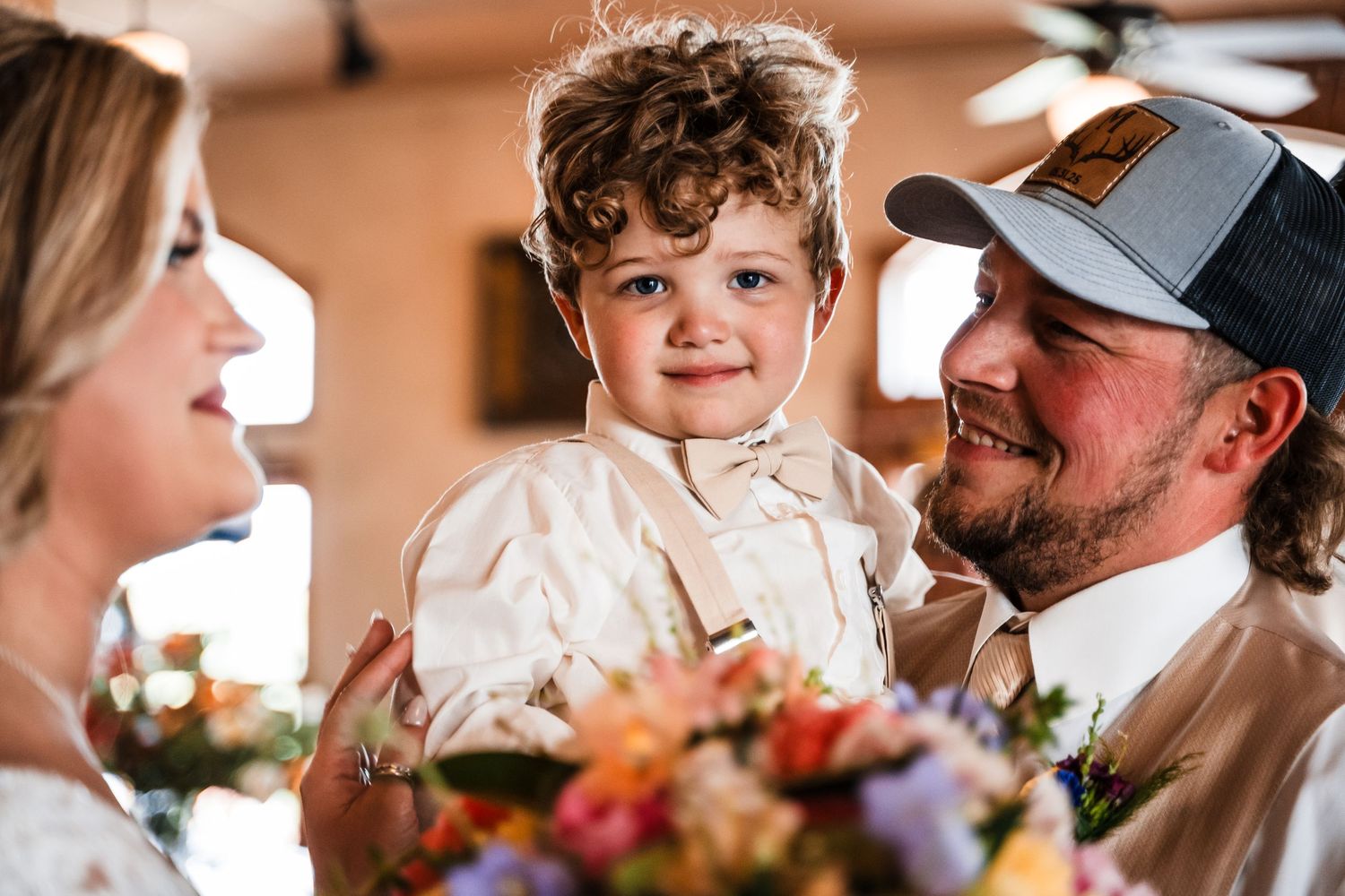 Three people share a joyful moment together at what appears to be a special event with floral decorations in the background.