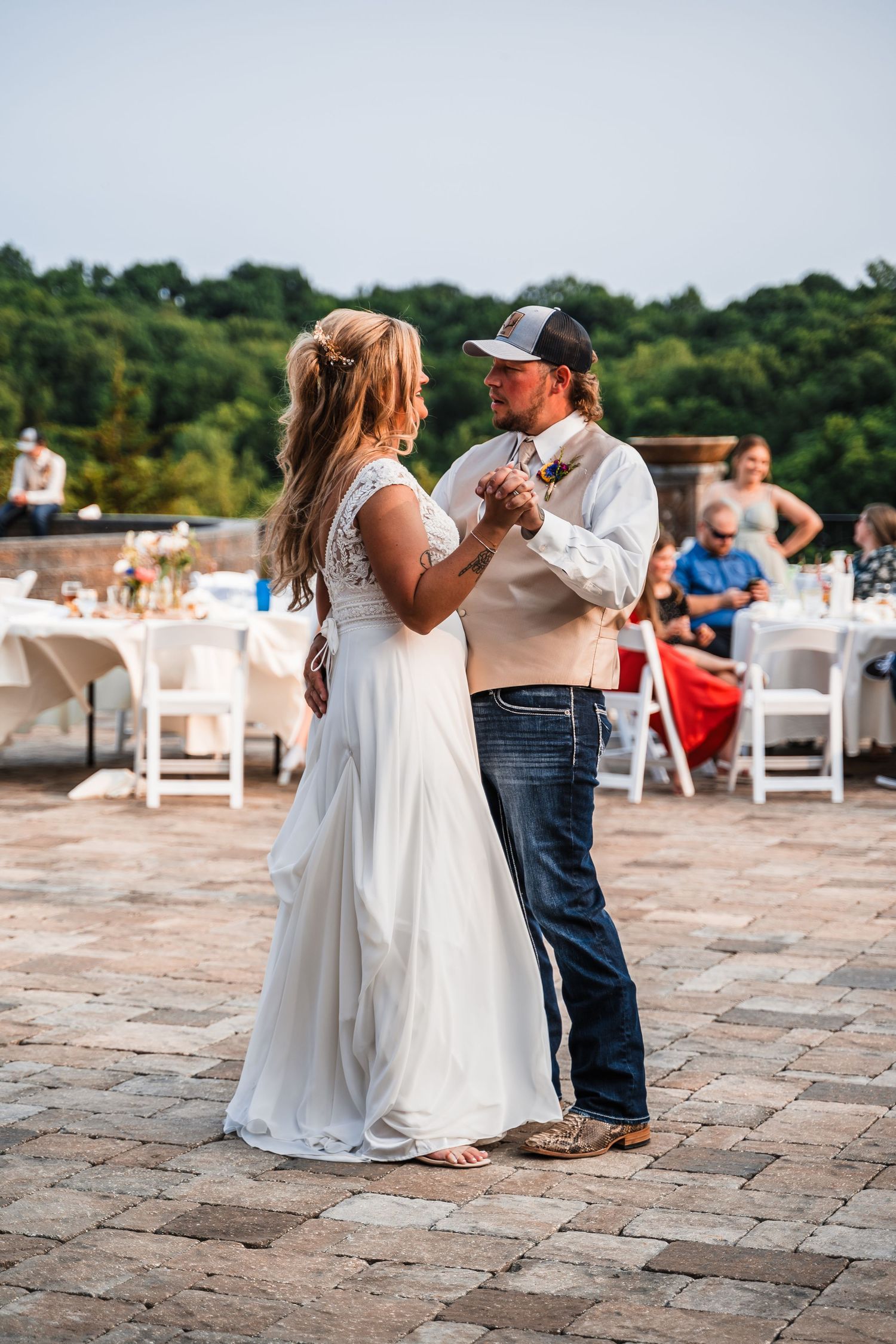 A couple shares a romantic dance on a stone patio with string lights overhead at a wedding reception.