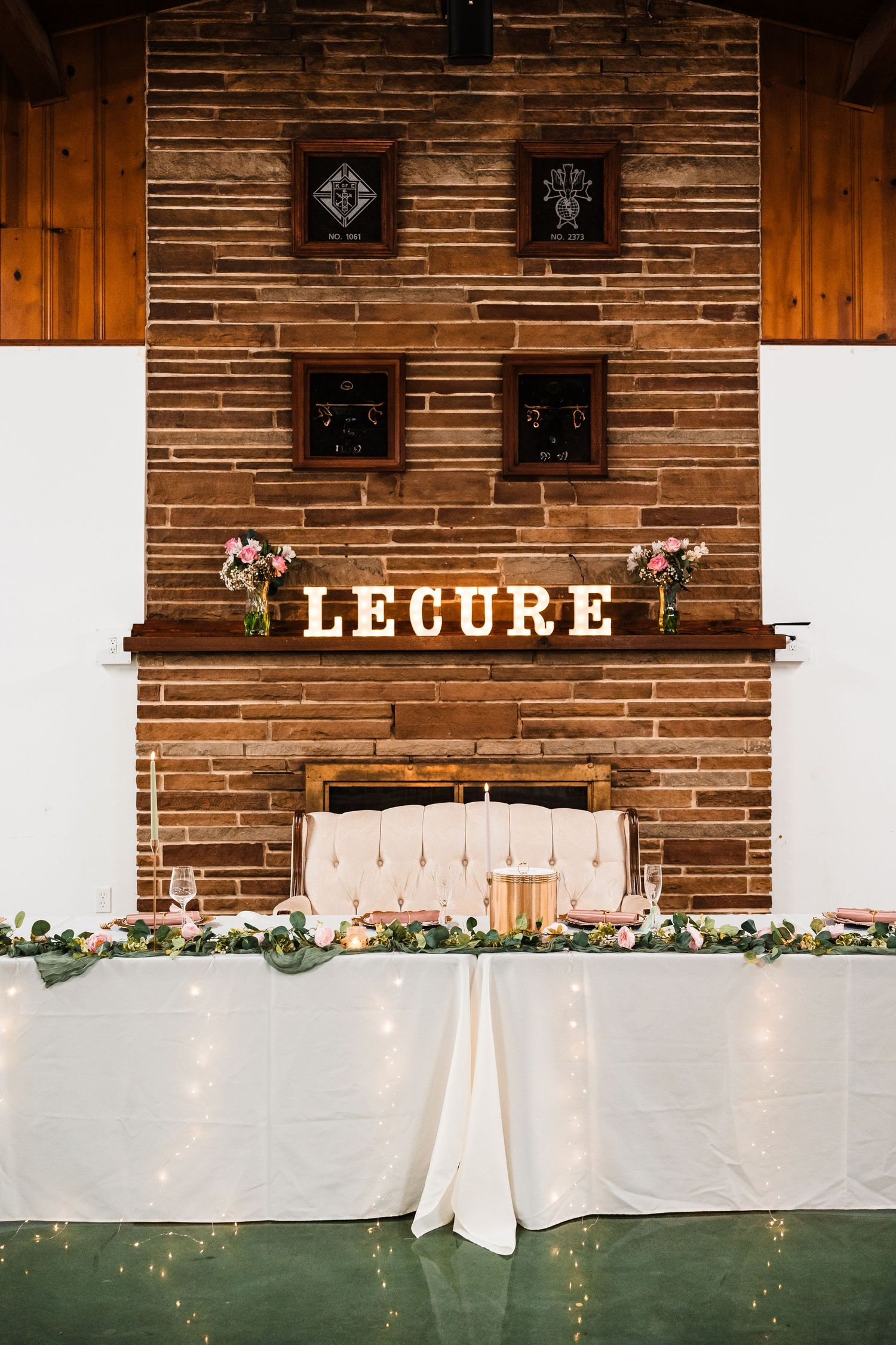 Rustic wooden wall decorated with 'LEGURE' signage and floral garlands at a wedding venue.