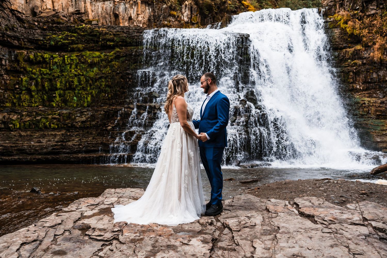 Couple posing for romantic wedding photos in front of a cascading waterfall.