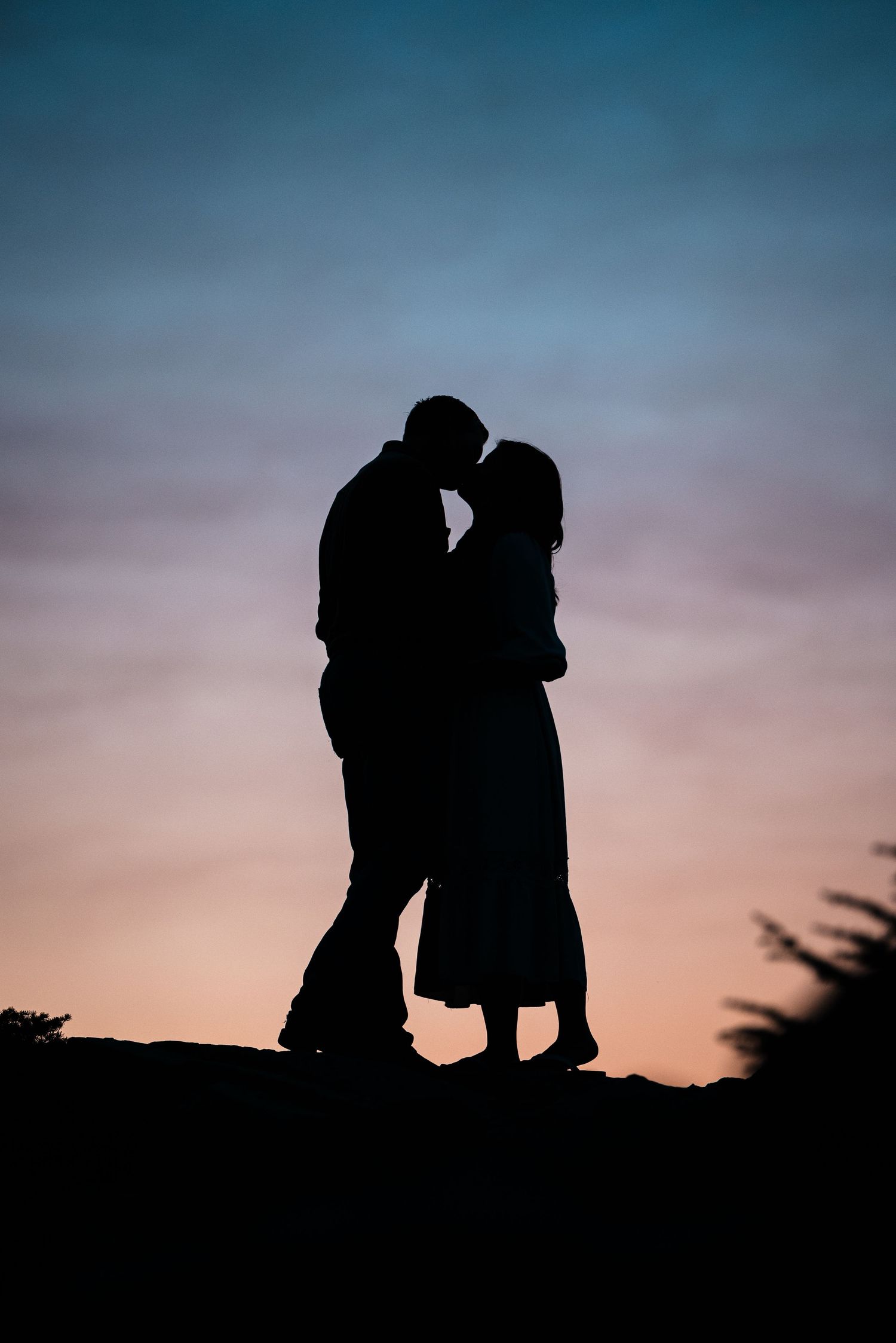 Two silhouetted figures stand close together against a dramatic sunset sky creating a romantic atmosphere.