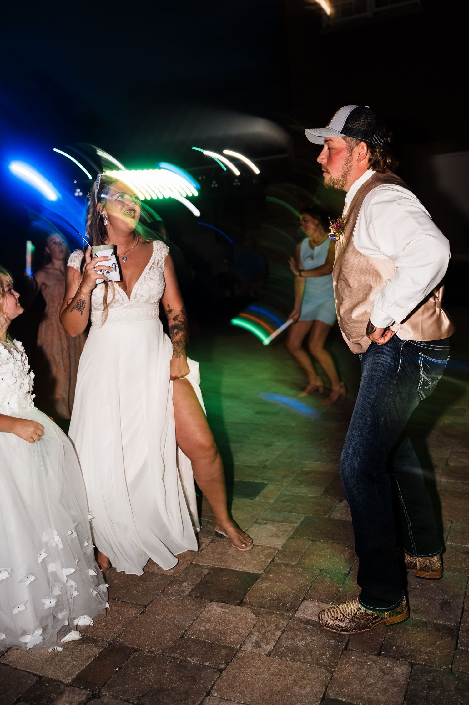 Wedding reception dance floor at night with colorful lights and guests dancing in casual attire.