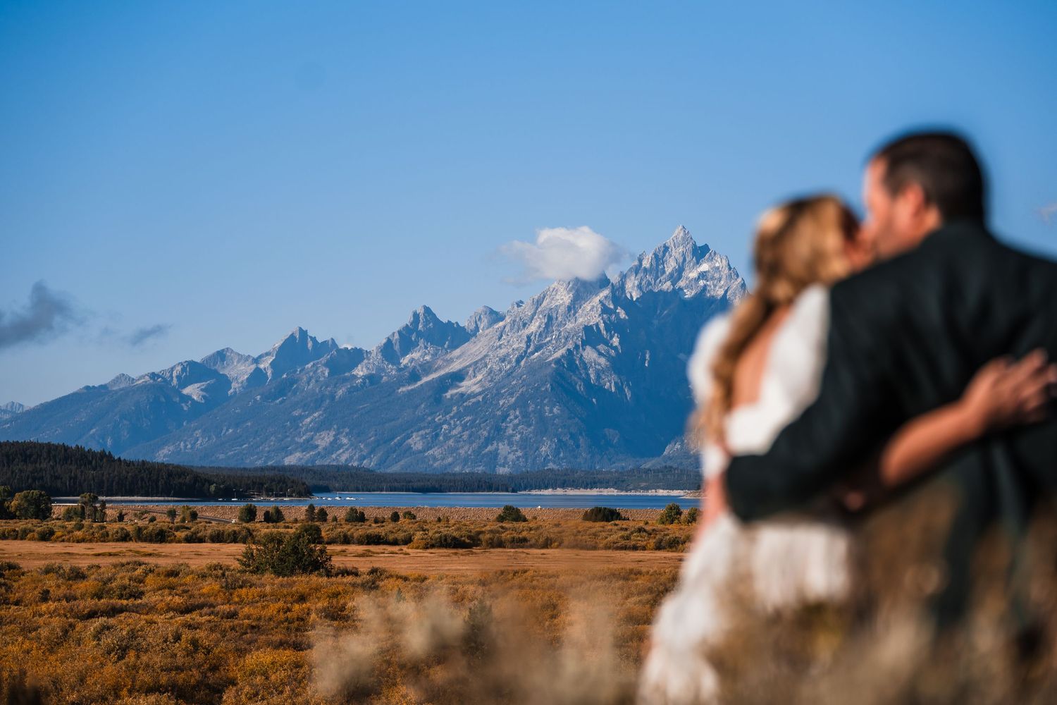 A panoramic view of the Grand Teton mountains with a couple in silhouette against the dramatic landscape.