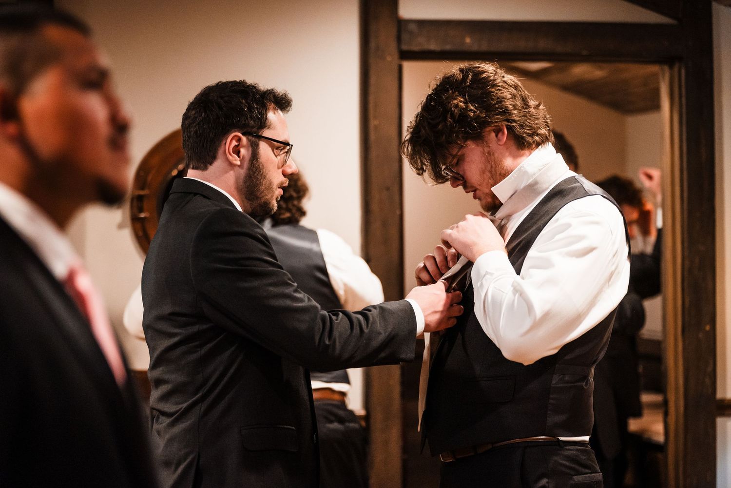 Groomsman helping groom adjust his tie before the wedding ceremony.