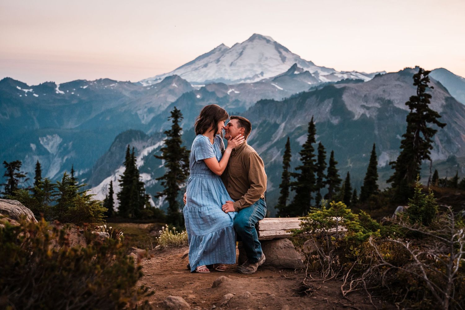 Two figures embrace while watching sunset over snow-capped Mount Baker in Washington's wilderness landscape.