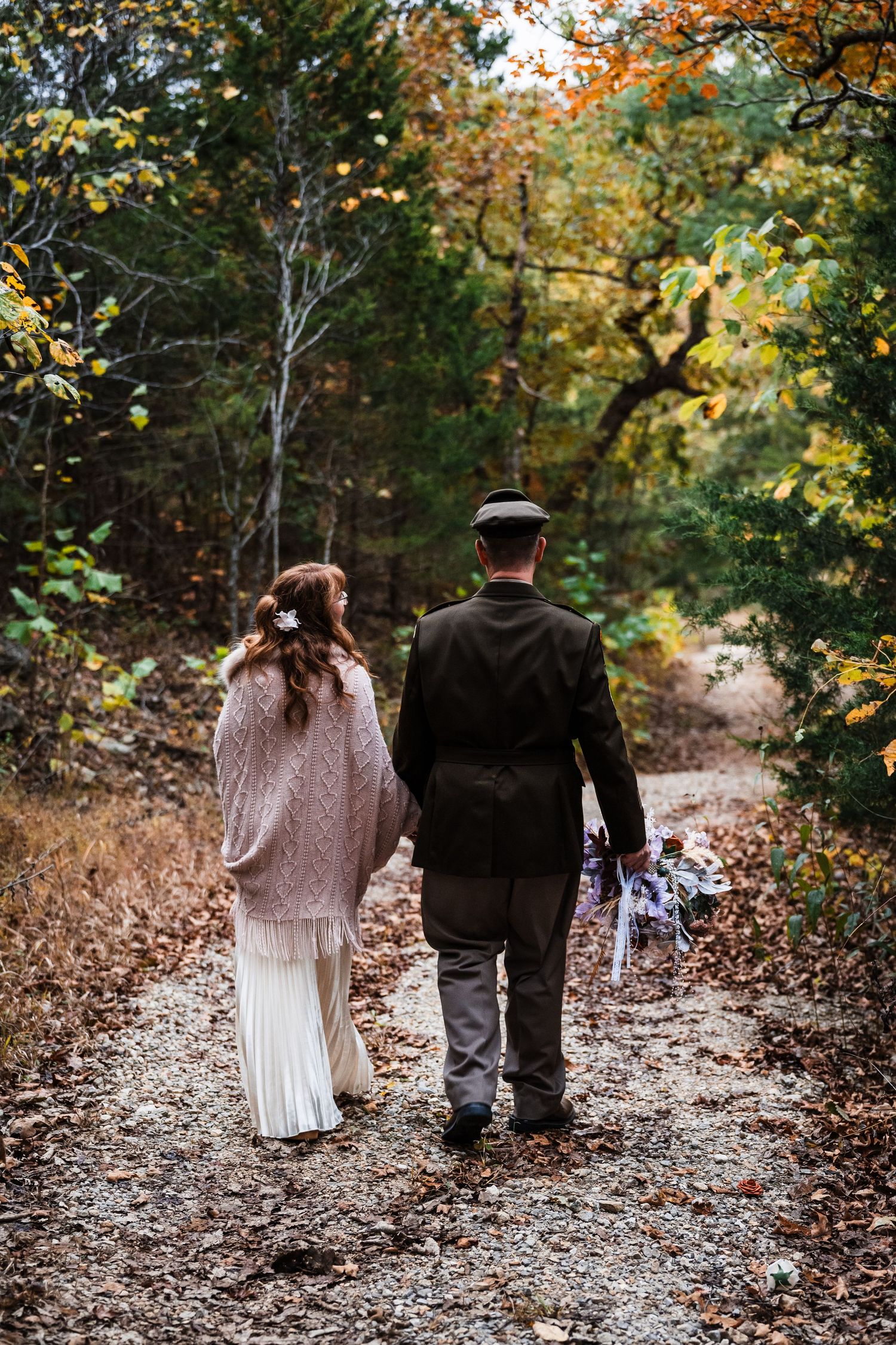 A couple walks hand in hand down a fall forest path after their wedding ceremony.
