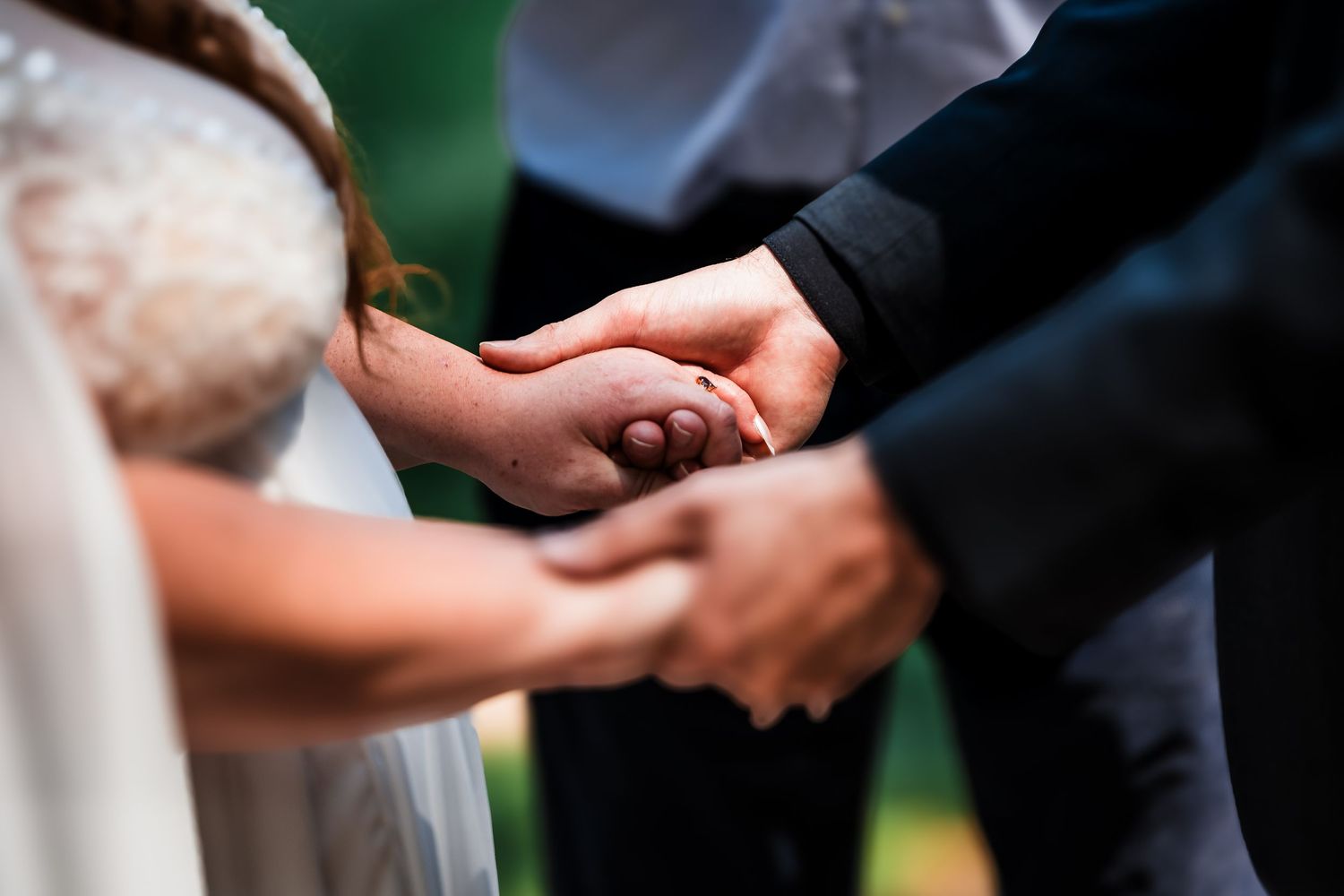 Wedding ceremony moment showing clasped hands of couple exchanging rings during intimate outdoor ceremony.