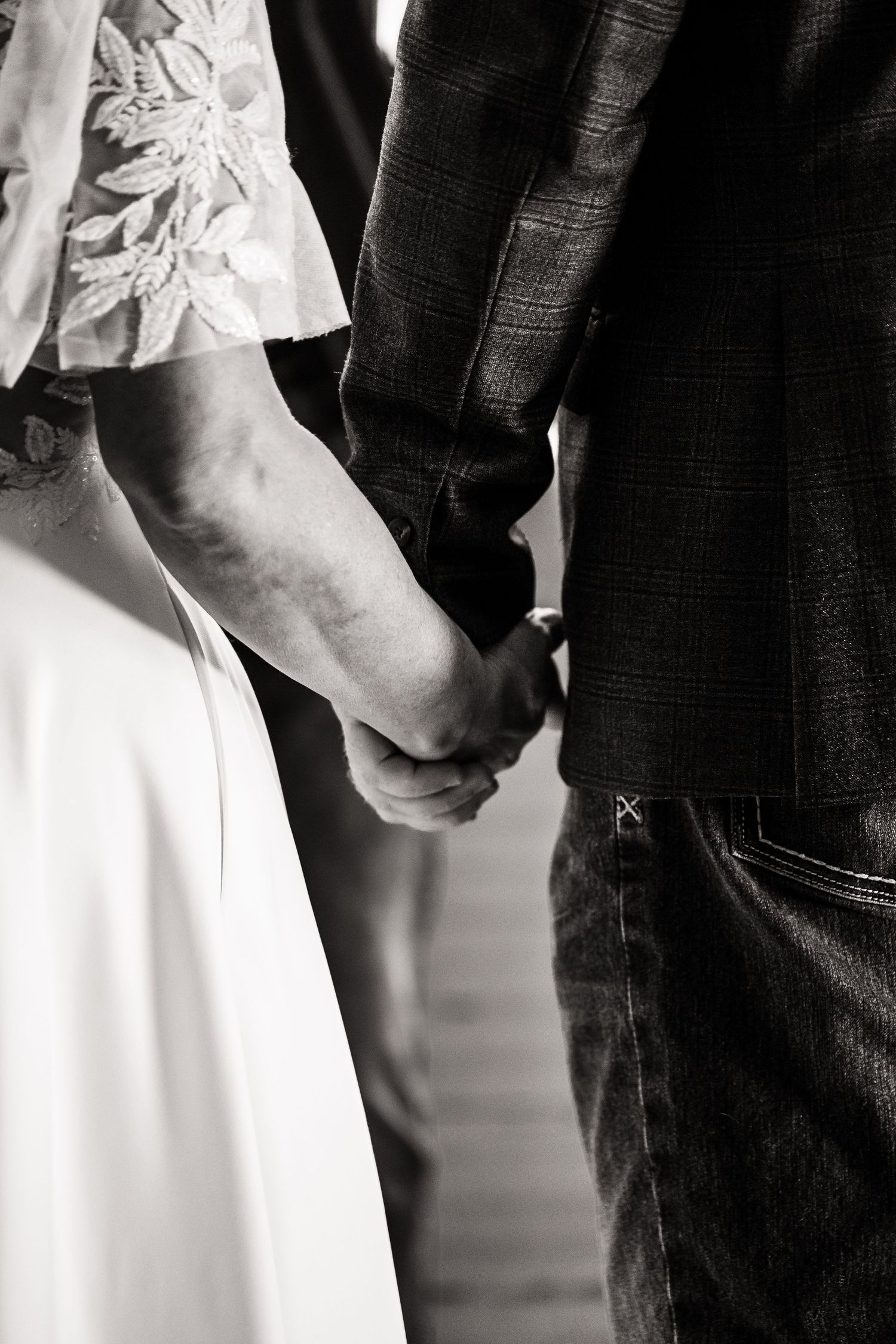 Close-up details of wedding couple showing white lace dress against dark suit and denim.