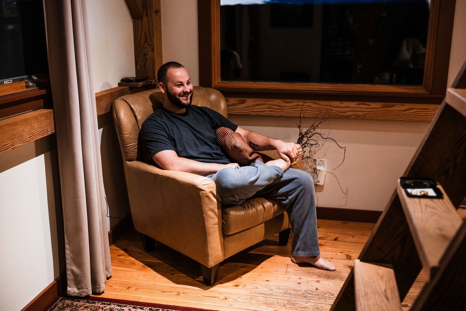 Person sitting on wooden floor at home using mobile device in dim lighting conditions.