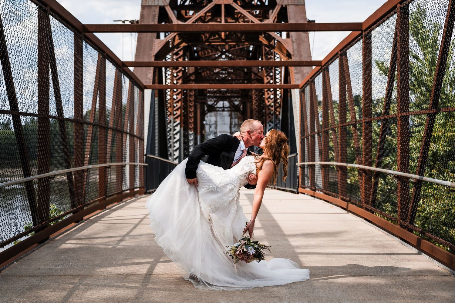 Wedding couple and bridal party pose on a rustic wooden bridge surrounded by trees.