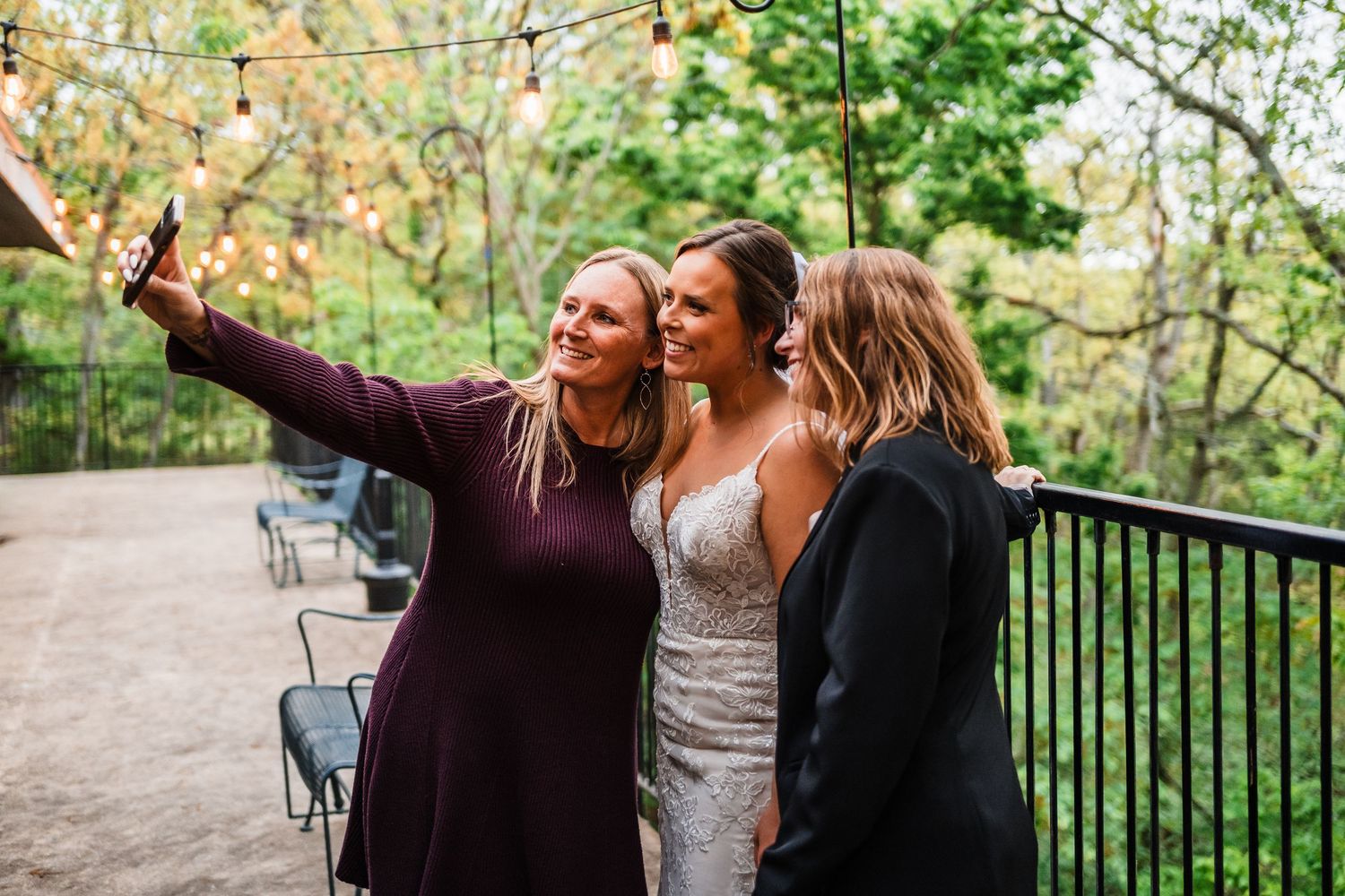 Three people pose together outdoors while taking a selfie on a patio at a special event.