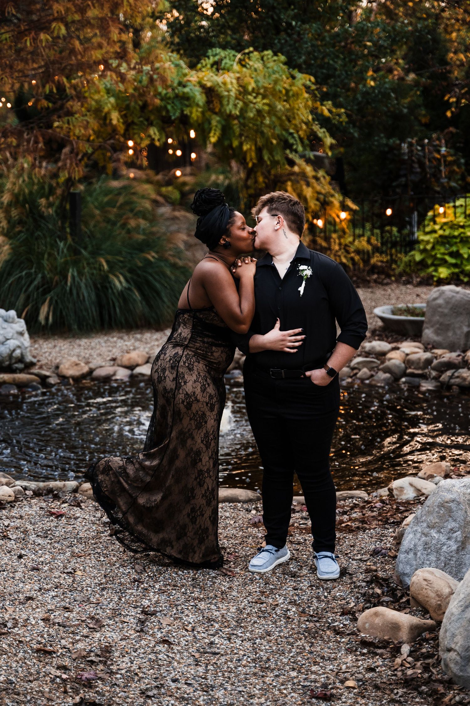Couple shares intimate moment in garden setting with string lights and natural landscaping.