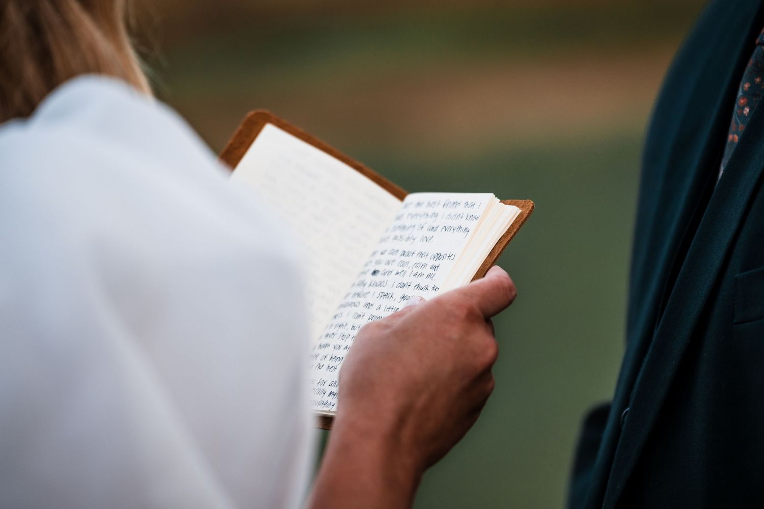 Wedding couple reading personal vows from paper during an outdoor ceremony.
